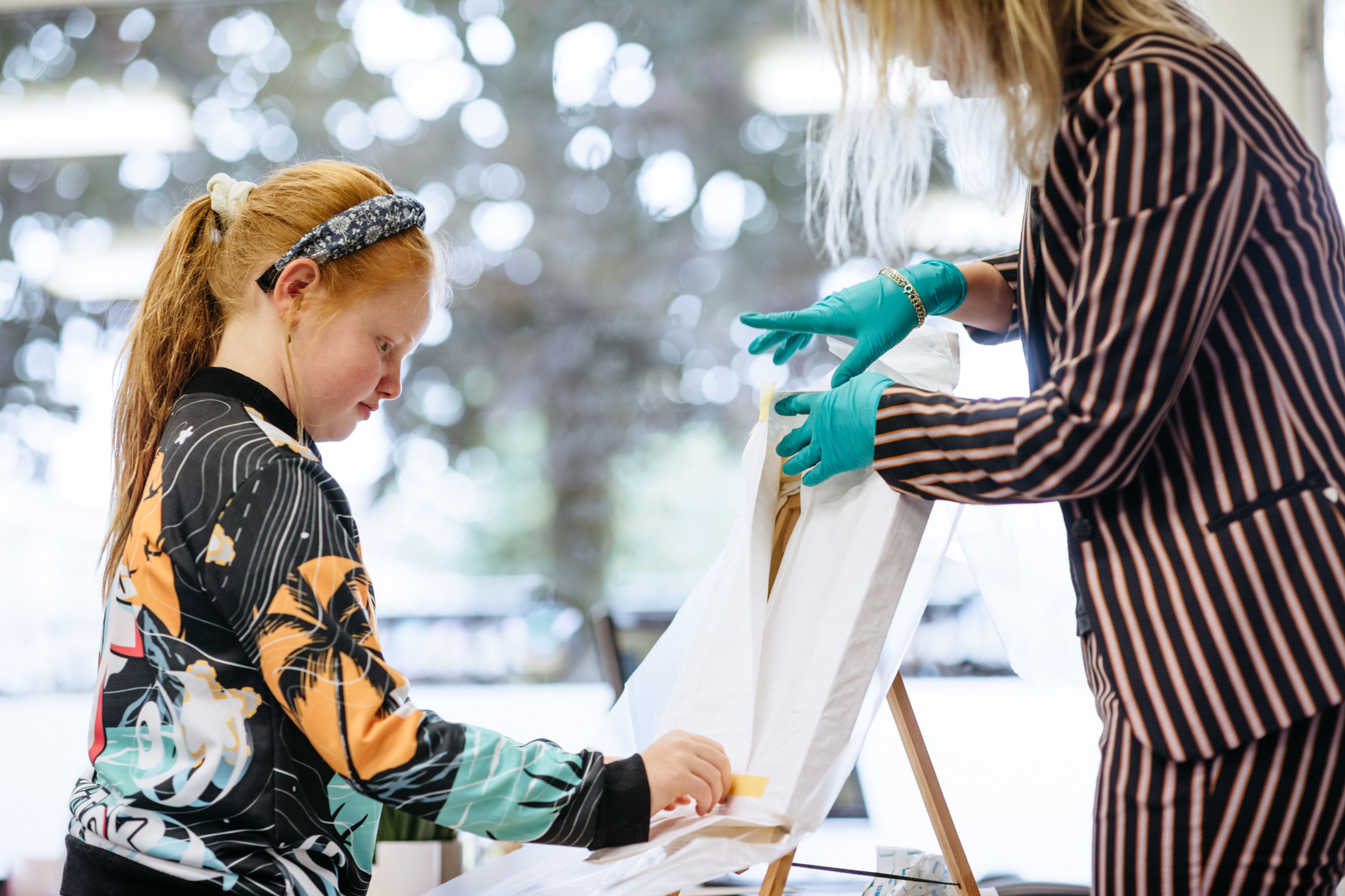 Leerling en museumdocent maken beschermfolie los van schilderij