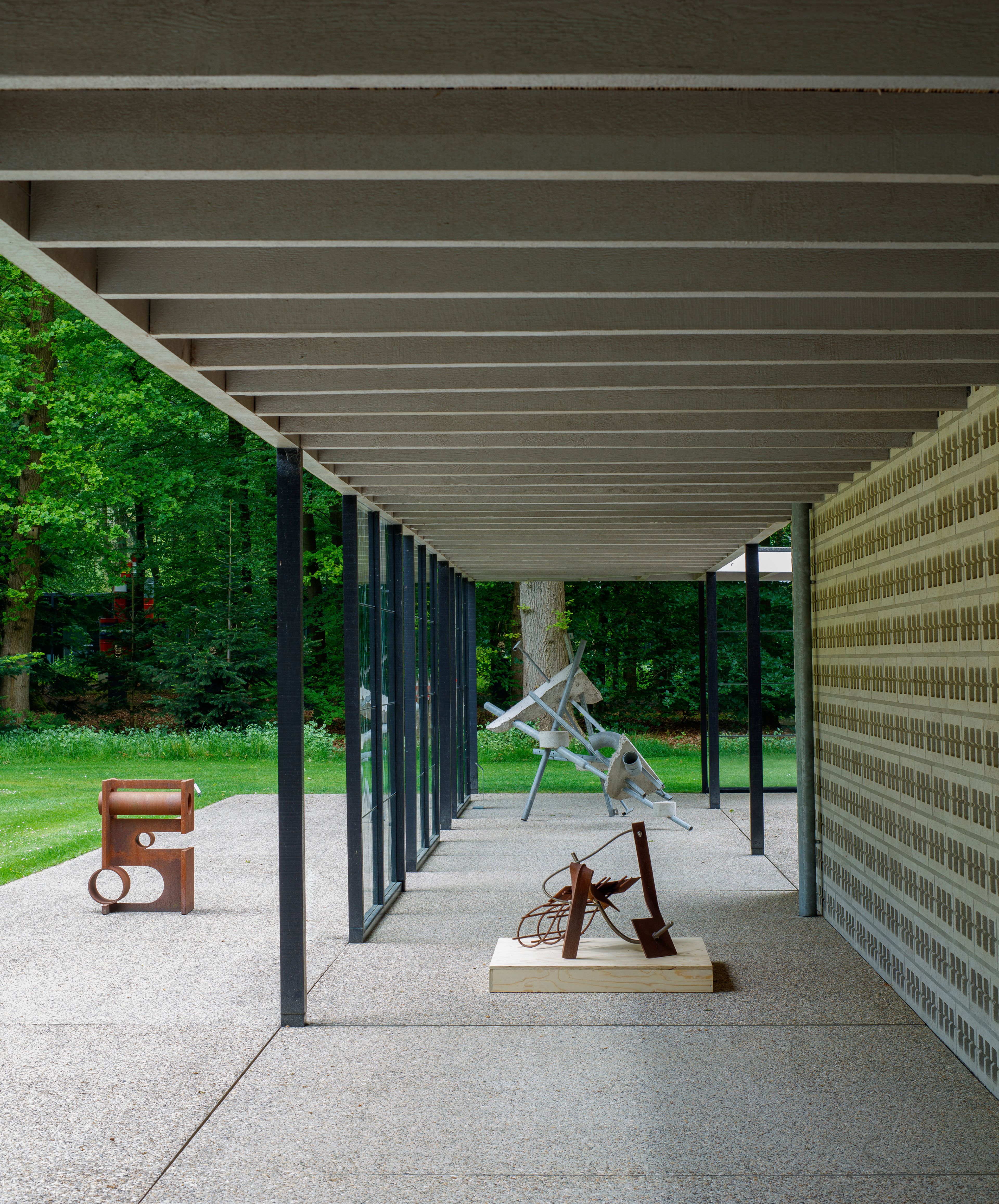 Ruud Kuijer in het Rietveldpaviljoen, foto: Rob Versluys Foto van een aantal beelden in staal in een modern paviljoen in een parkachtige omgeving. De beelden hebben grillige vormen