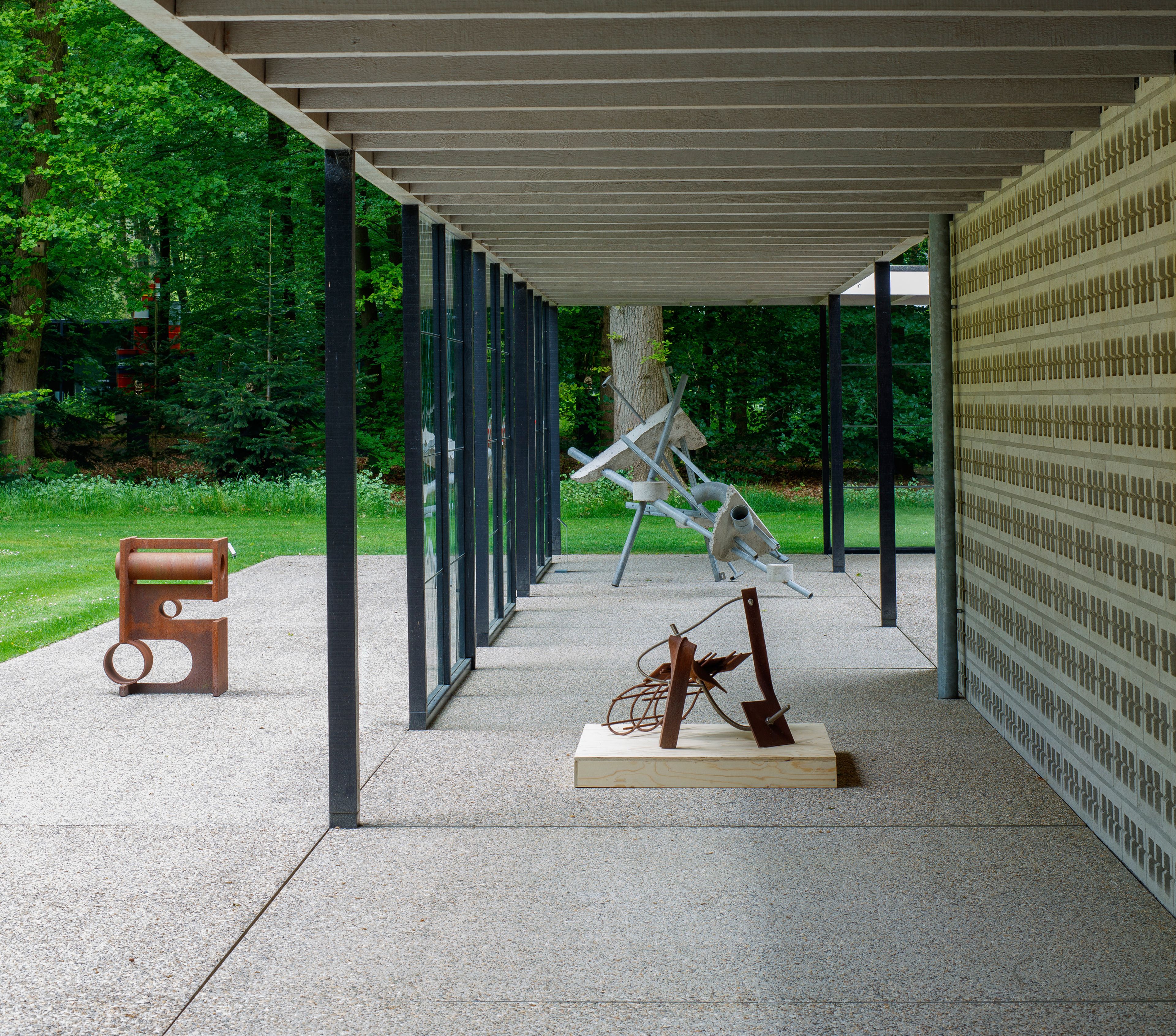 Ruud Kuijer in het Rietveldpaviljoen, foto: Rob Versluys Foto van een aantal beelden in staal in een modern paviljoen in een parkachtige omgeving. De beelden hebben grillige vormen