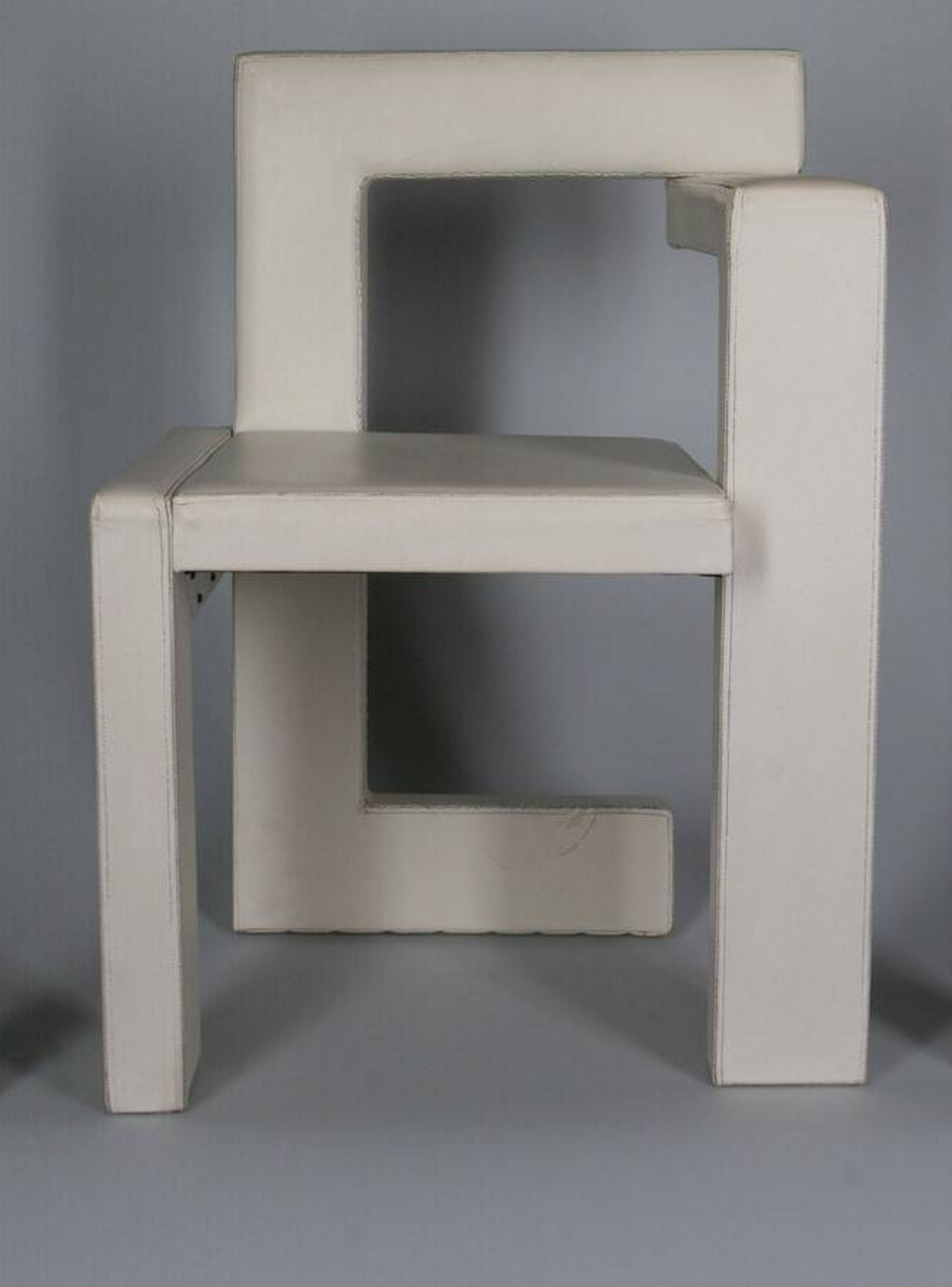 Gerrit Rietveld, 'Steltman stoel' (originele versie voor de juwelierszaak Steltman), 1963 Foto van een moderne stoel met een bijzonder, hoekig ontwerp in witte bekleding. Stoel heeft rechte lijnen en open ruimtes, wat een minimalistische en architectonische uitstraling geeft.