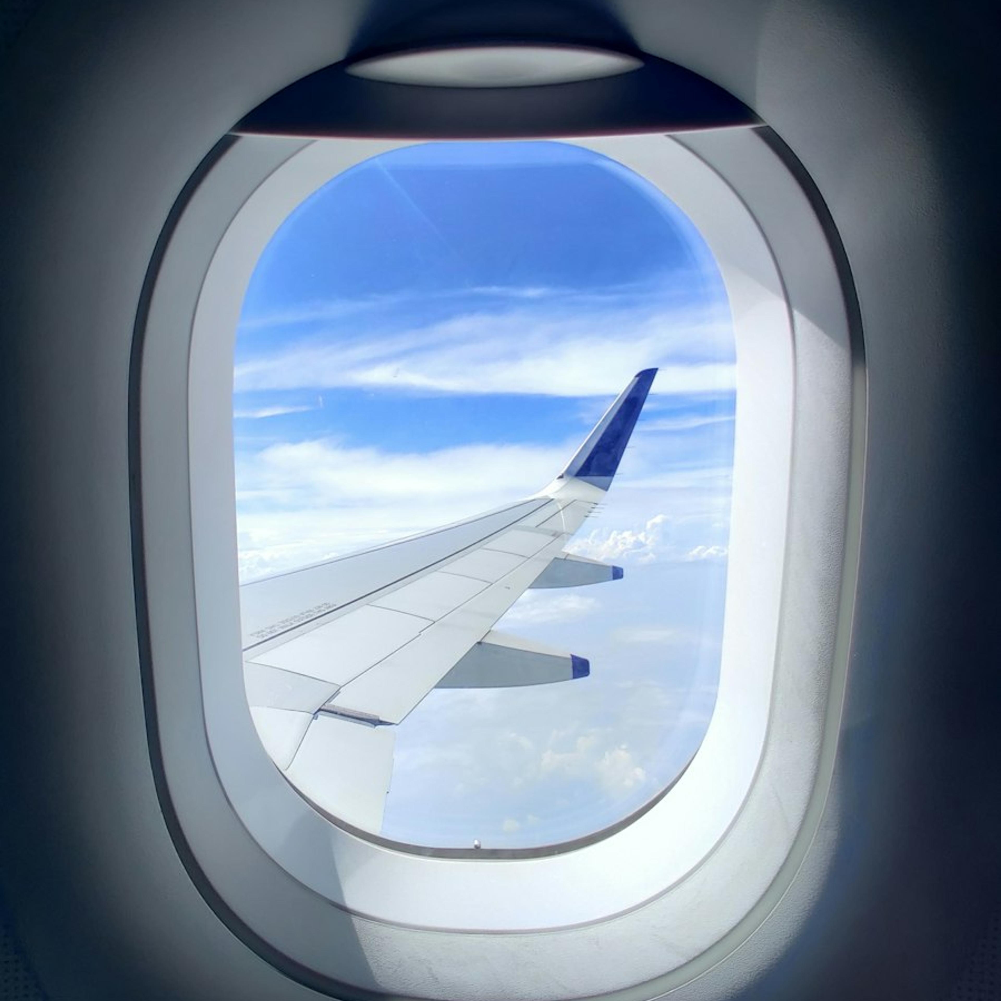 An airplane wing seen through the window, above the clouds