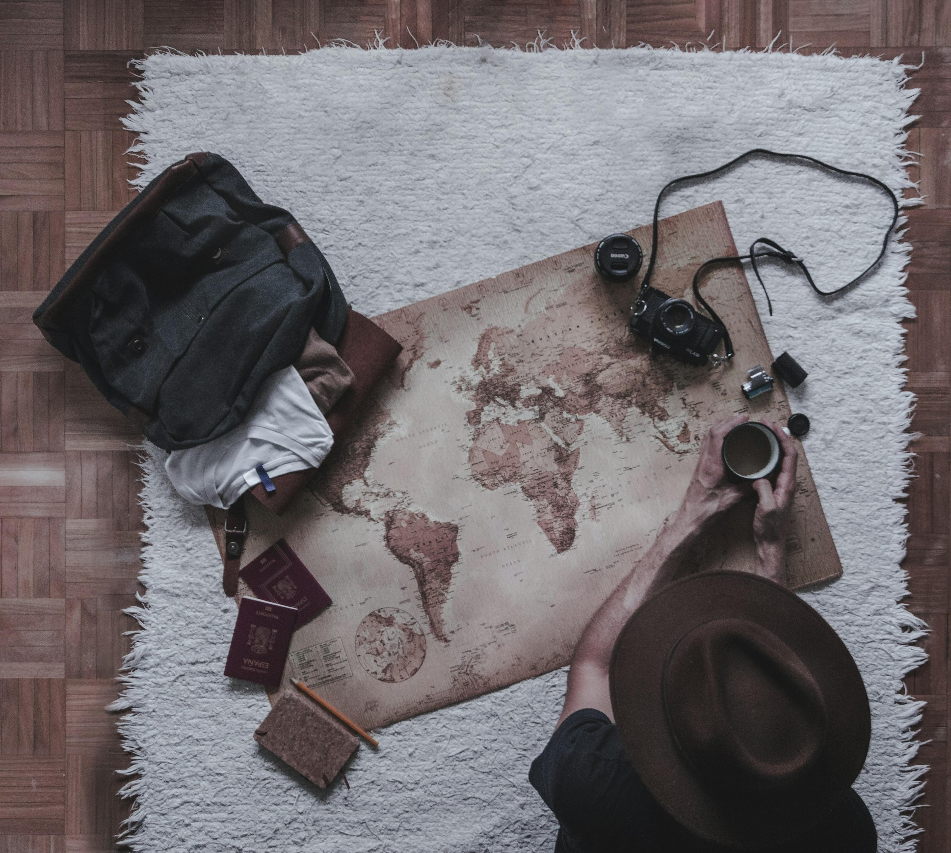 Une main tient une tasse de café à côté d'une carte du monde et d'un appareil photo