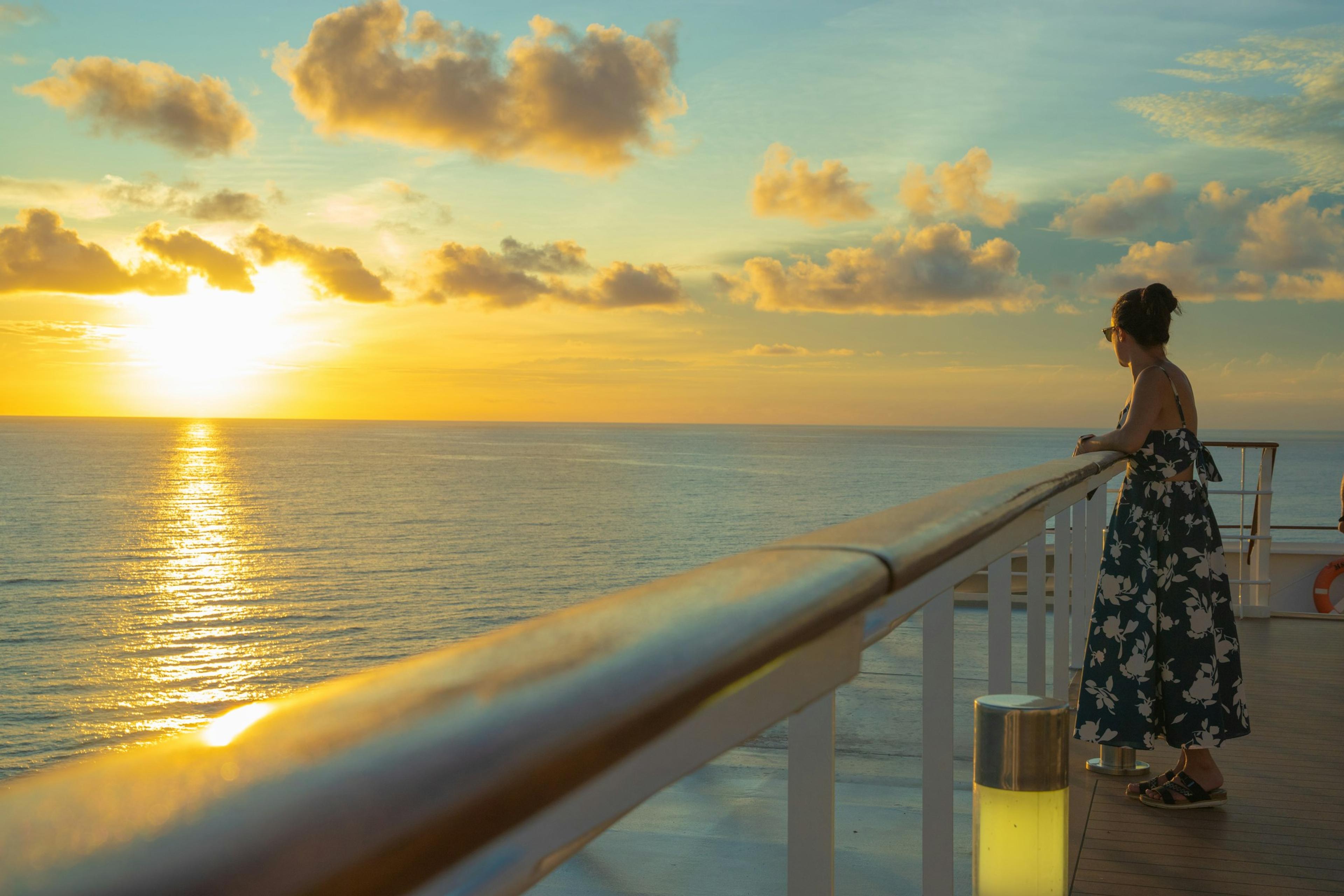 Une voyageuse accoudée au bastingage d'un navire de croisière, face au soleil couchant