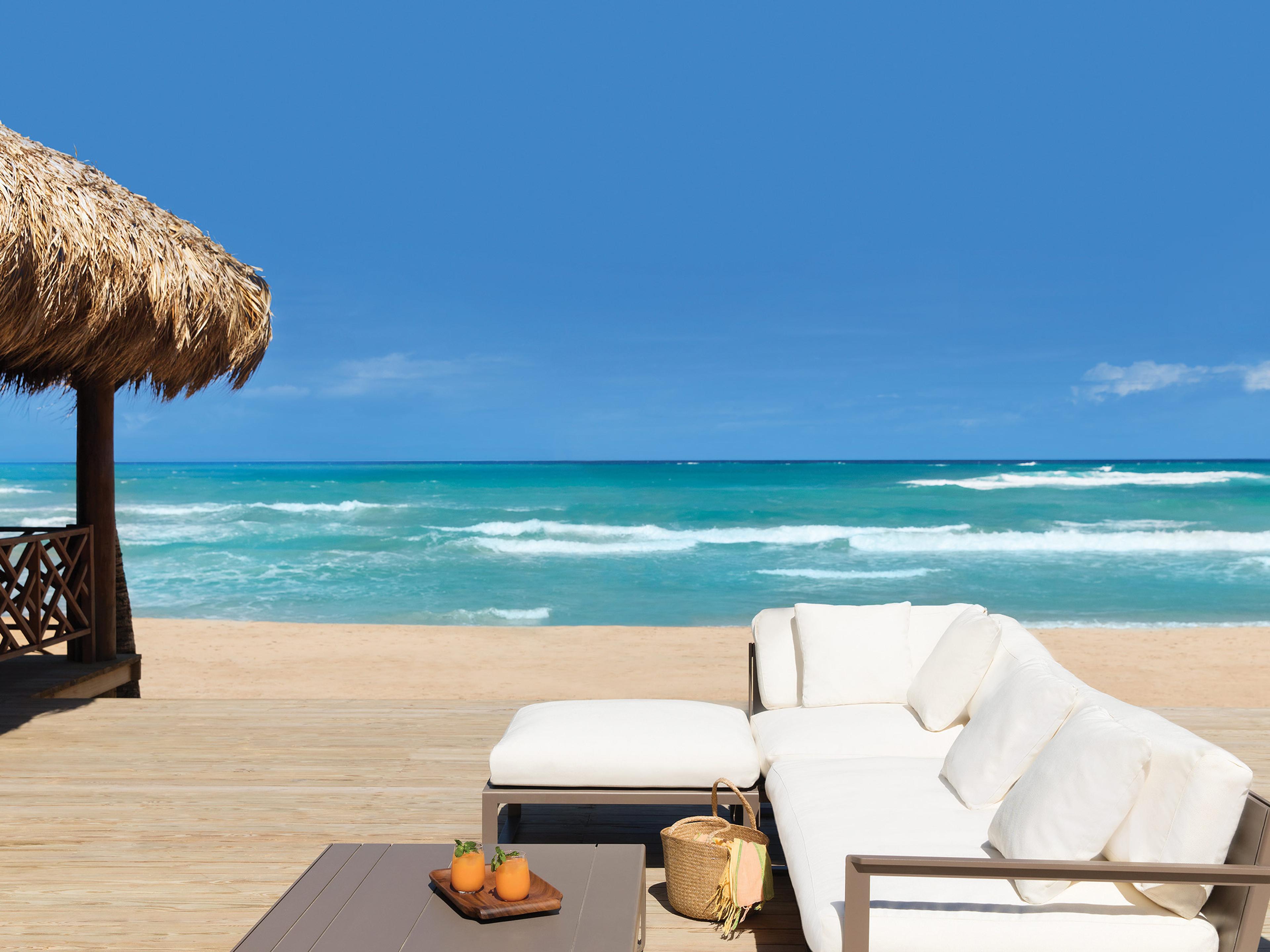 Des lits de plage blancs sous une paillote, face à la mer, à l'Excellence Punta Cana
