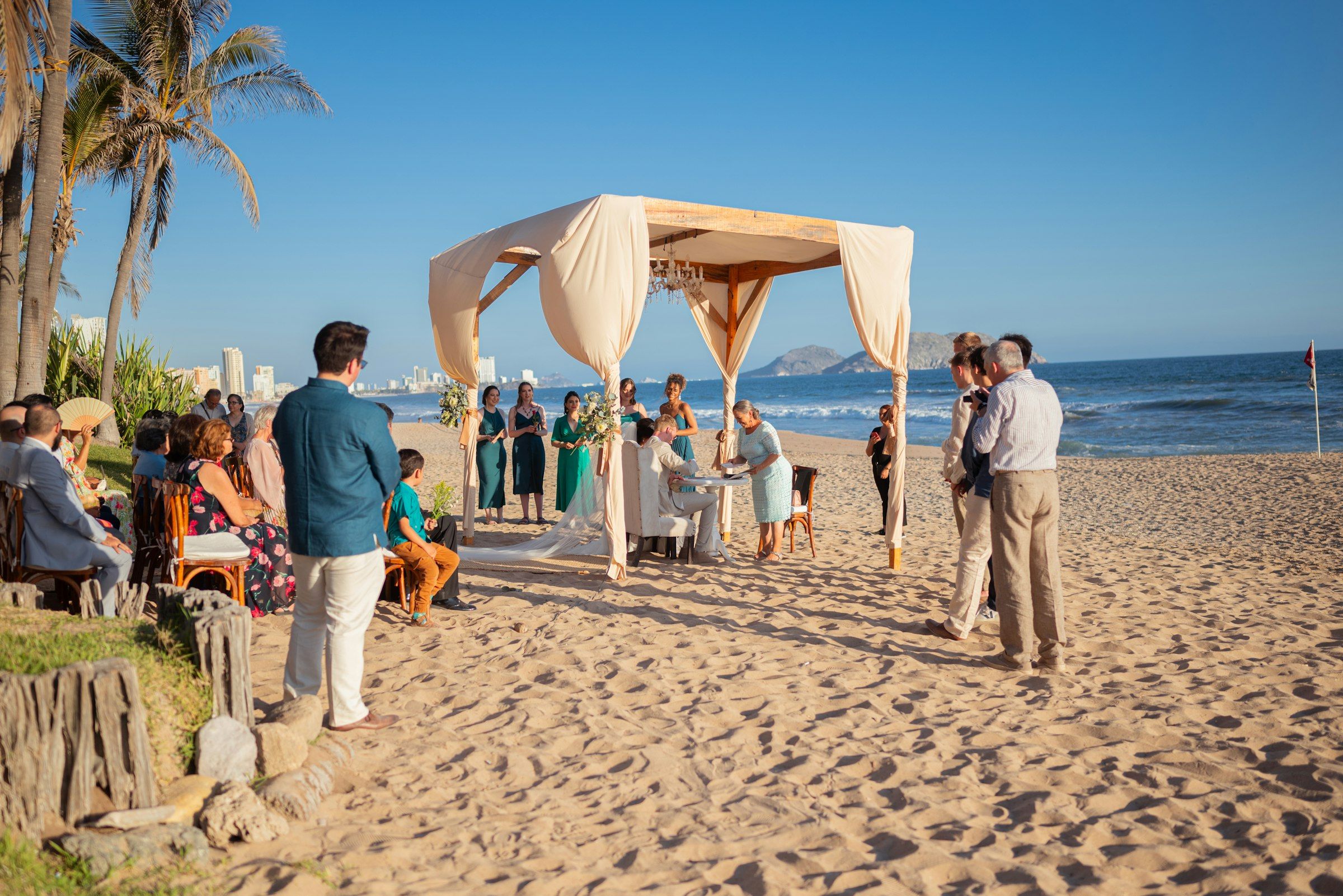 A beach wedding ceremony with guests under a canopy