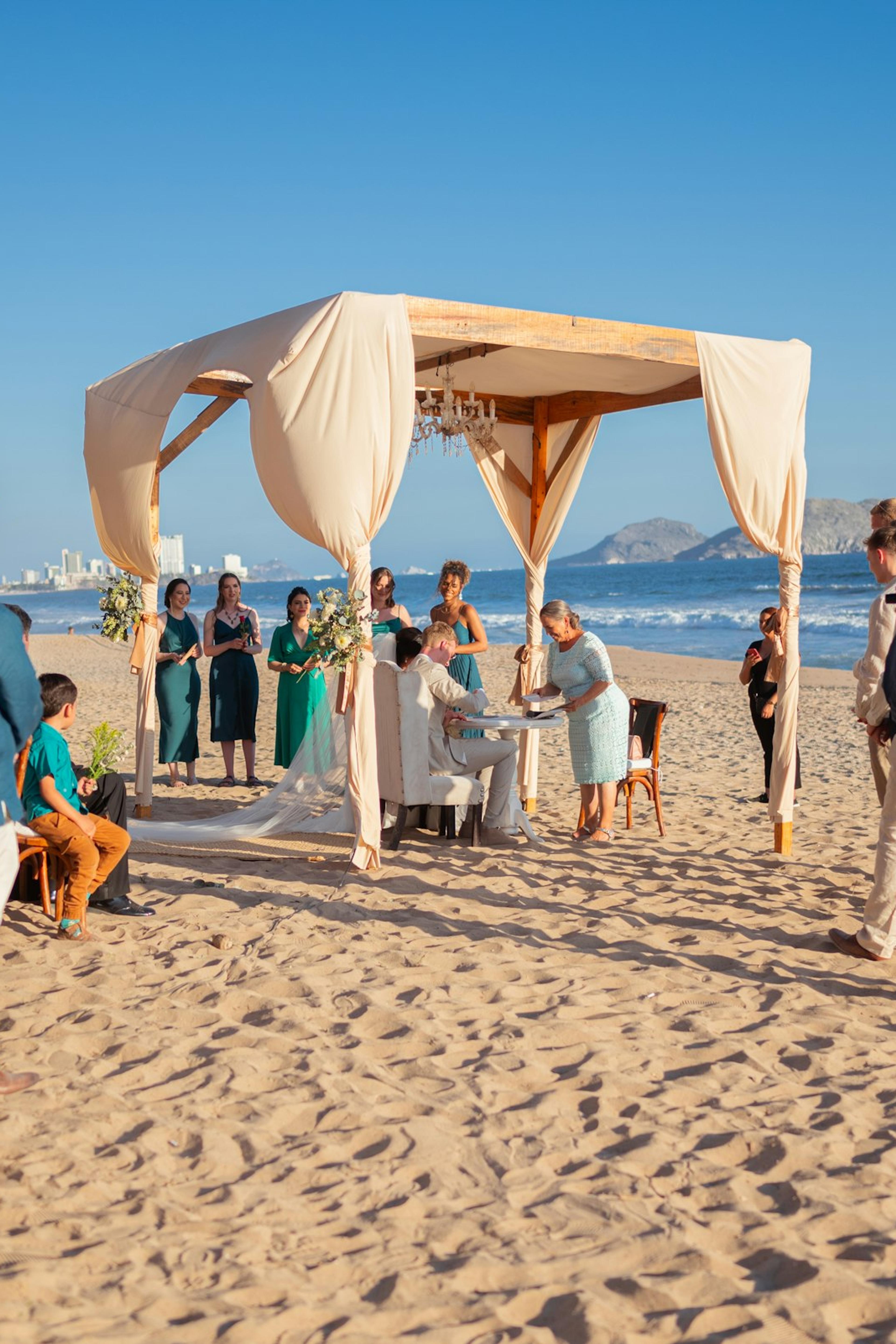 A beach wedding ceremony with guests under a canopy