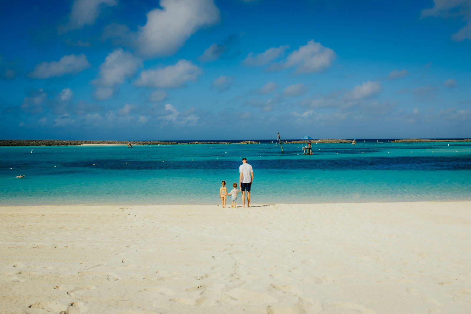 Un adulte et deux enfants marchent au bord de l'eau, sur une plage des Bahamas