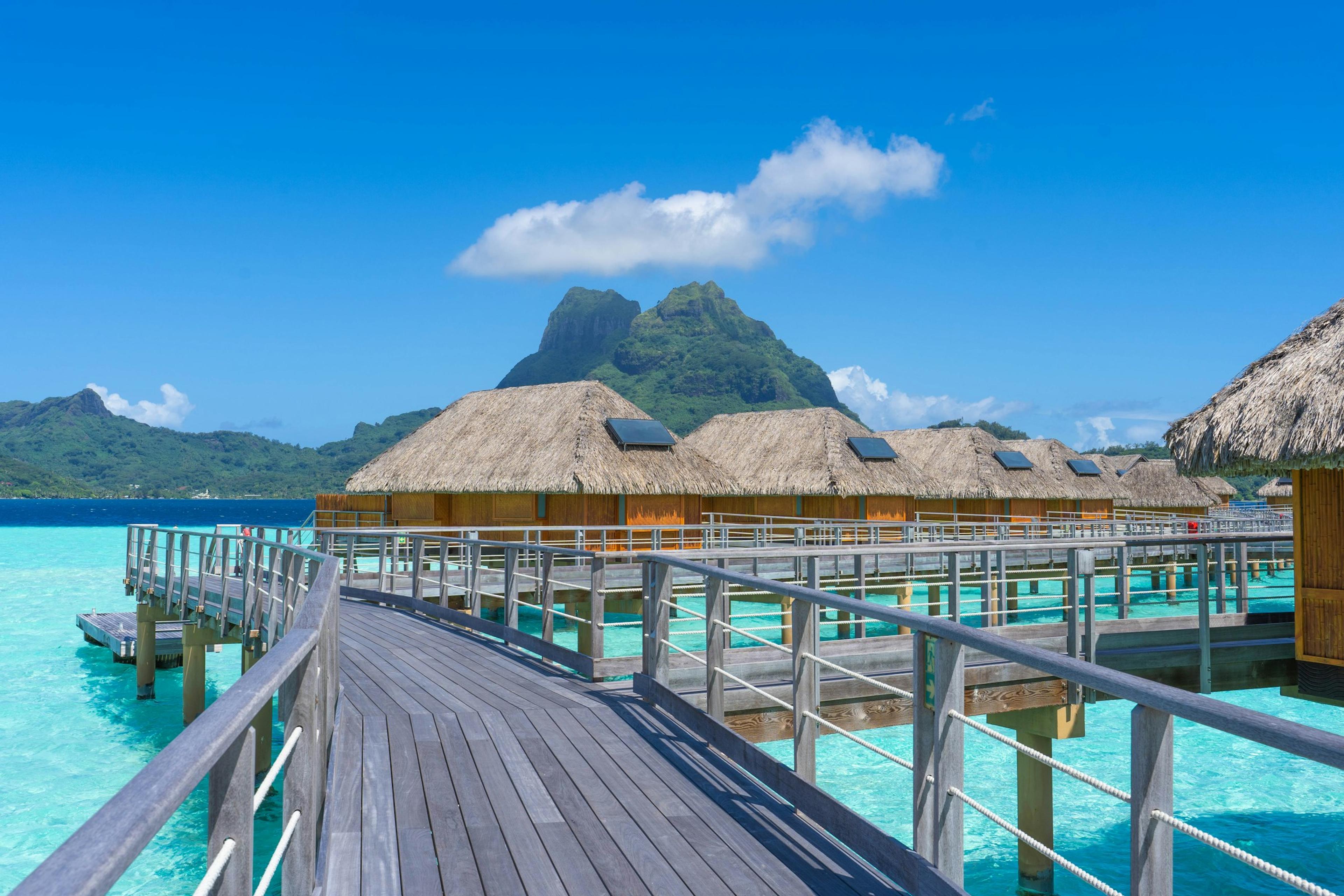 Overwater bungalows in a lagoon, in front of a mountain