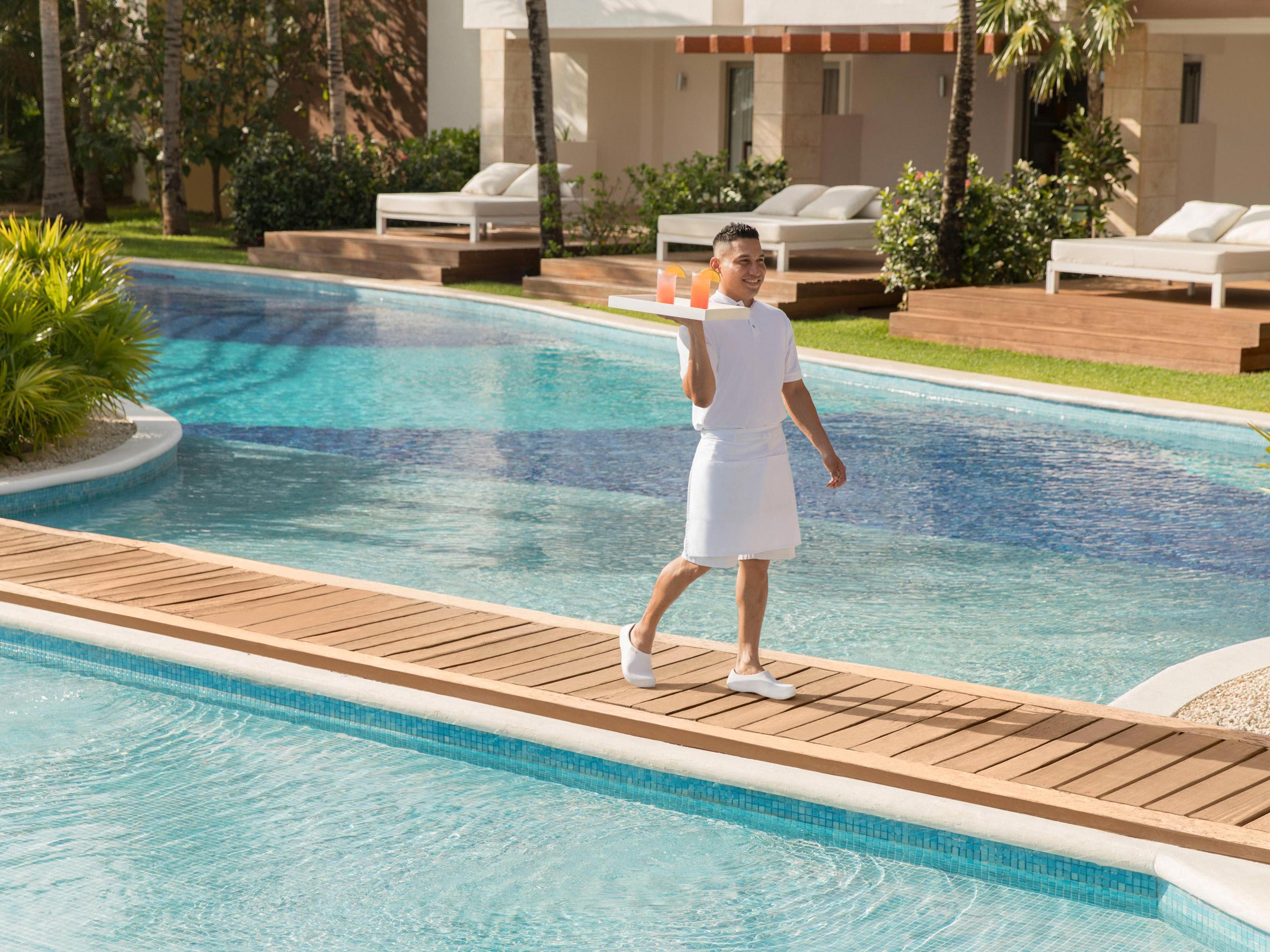 Un serveur traverse la passerelle d'une piscine de l'Excellence Playa Mujeres, plateau à la main