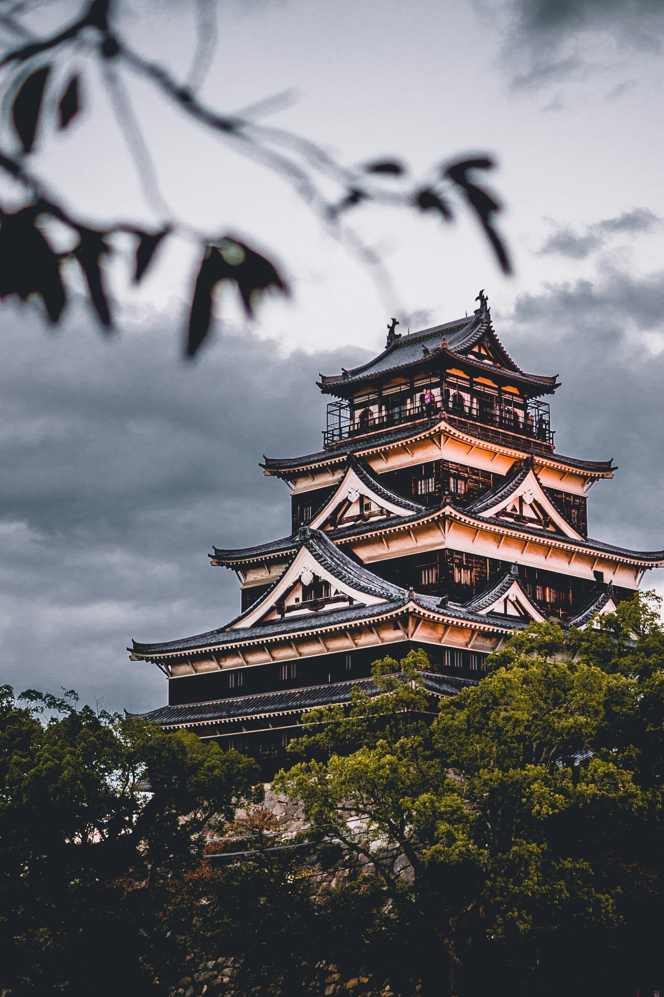 Un château japonais entre les arbres, sous un ciel d'orage