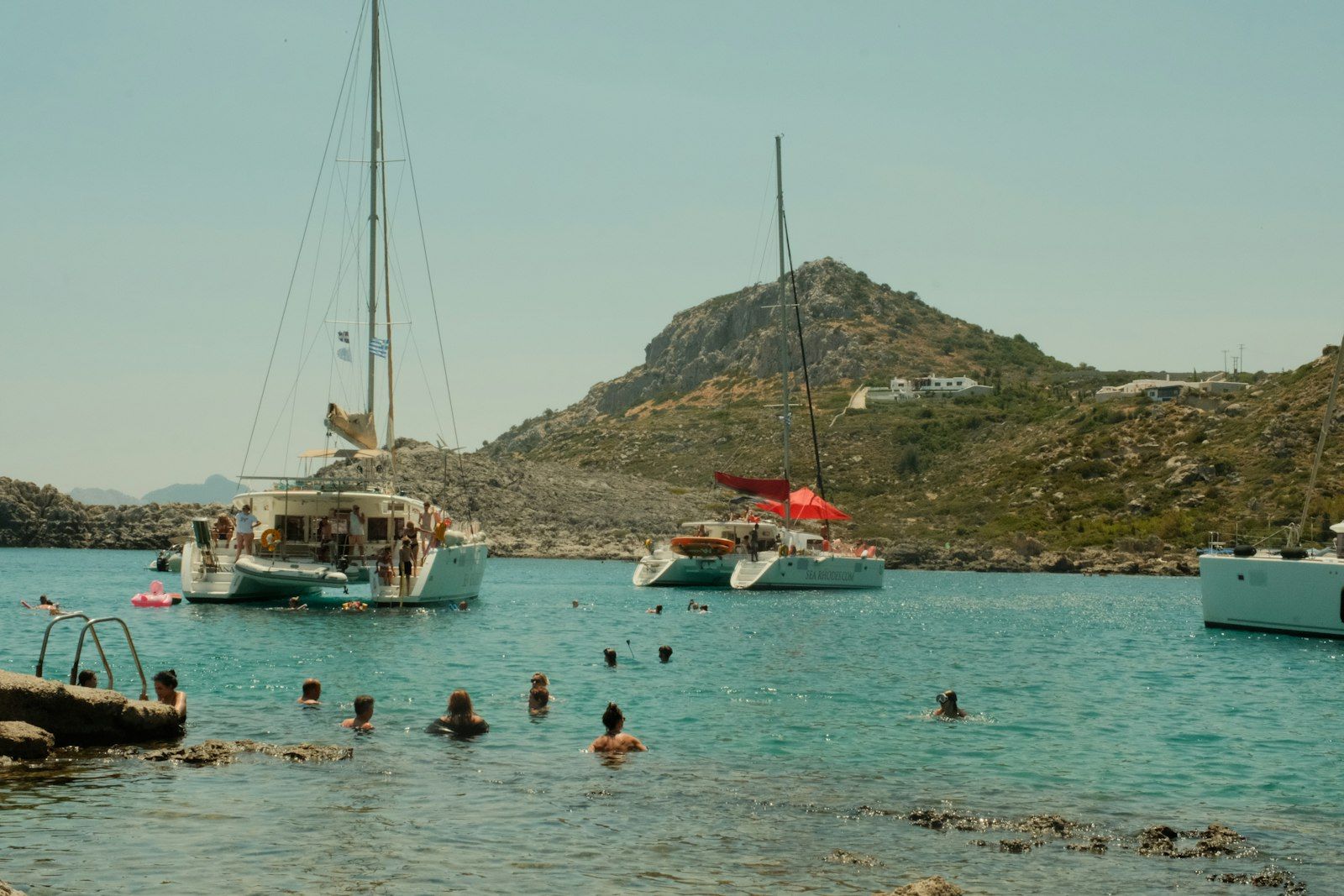 Des baigneurs autour de catamarans au mouillage, dans une baie grecque