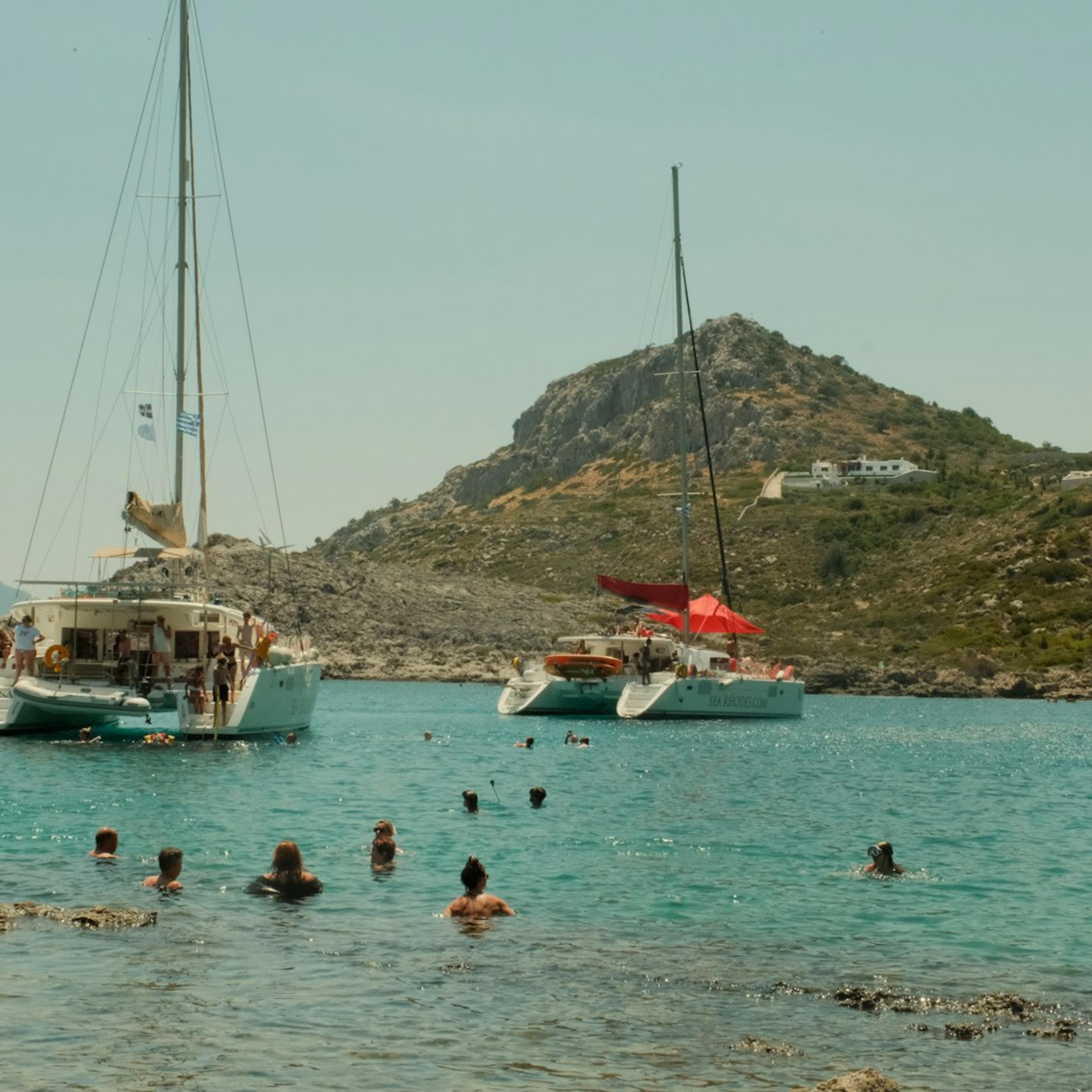 Des baigneurs autour de catamarans au mouillage, dans une baie grecque