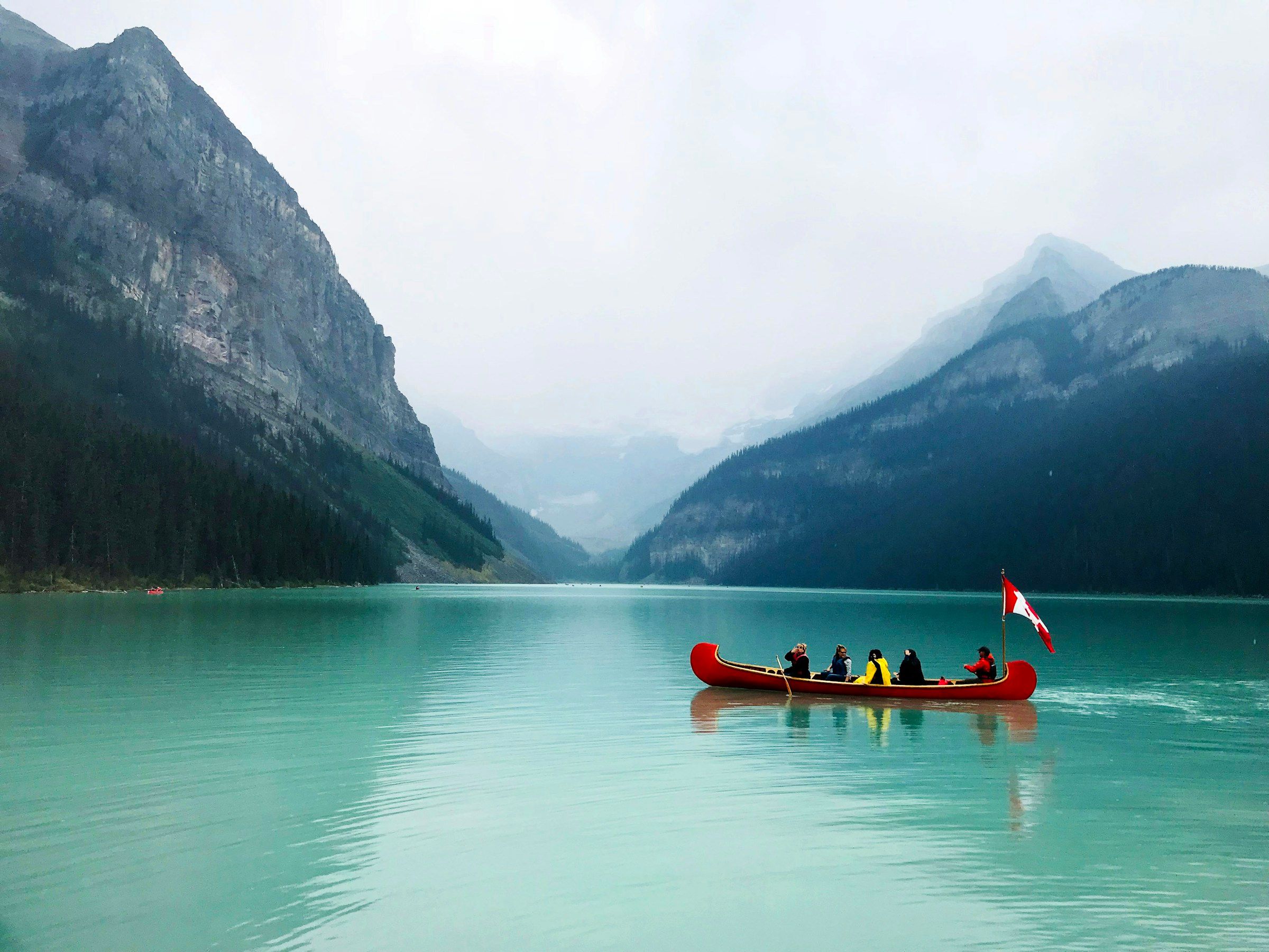 Un canot rouge chargé de voyageurs sur le lac Louise, au pied des montagnes