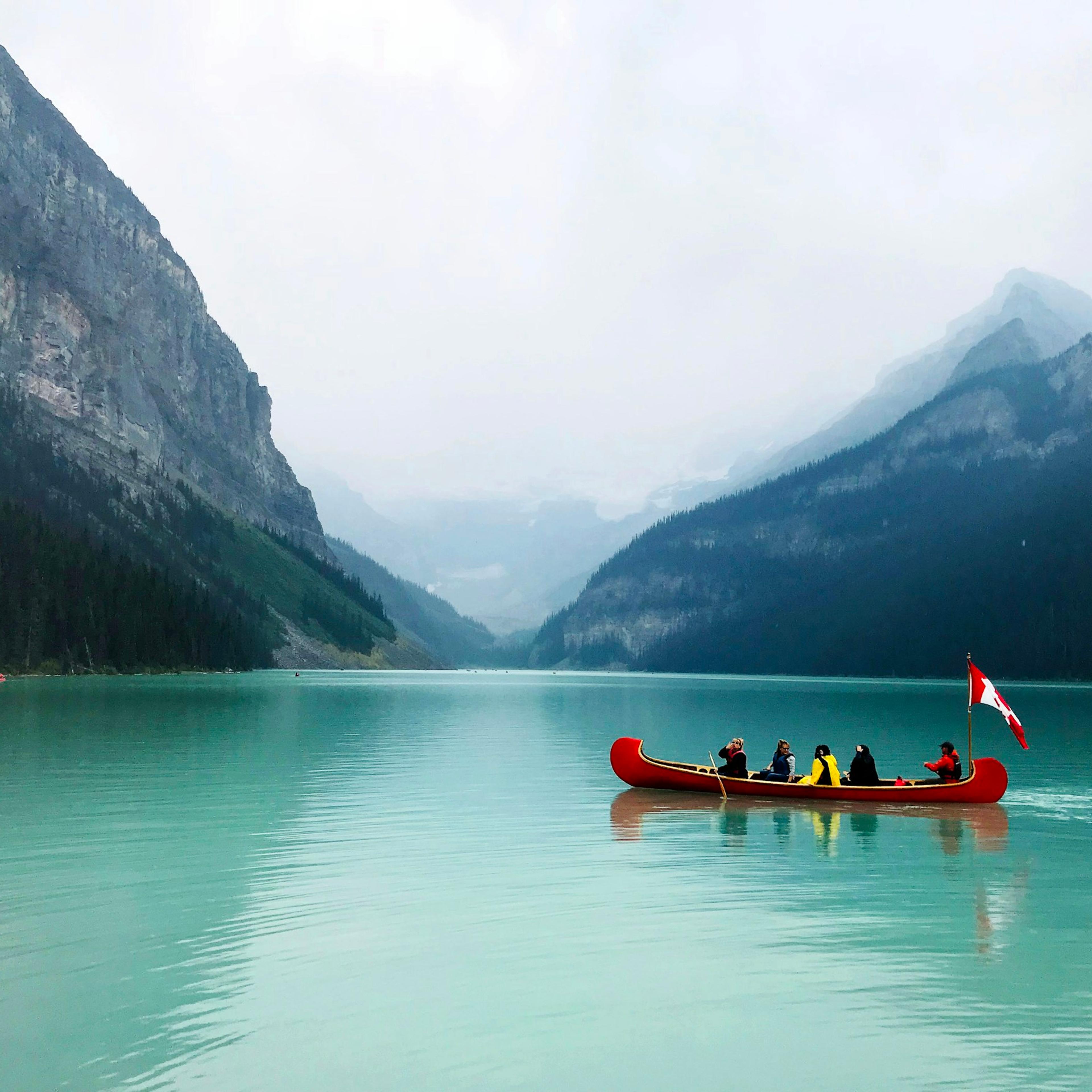 Un canot rouge chargé de voyageurs sur le lac Louise, au pied des montagnes