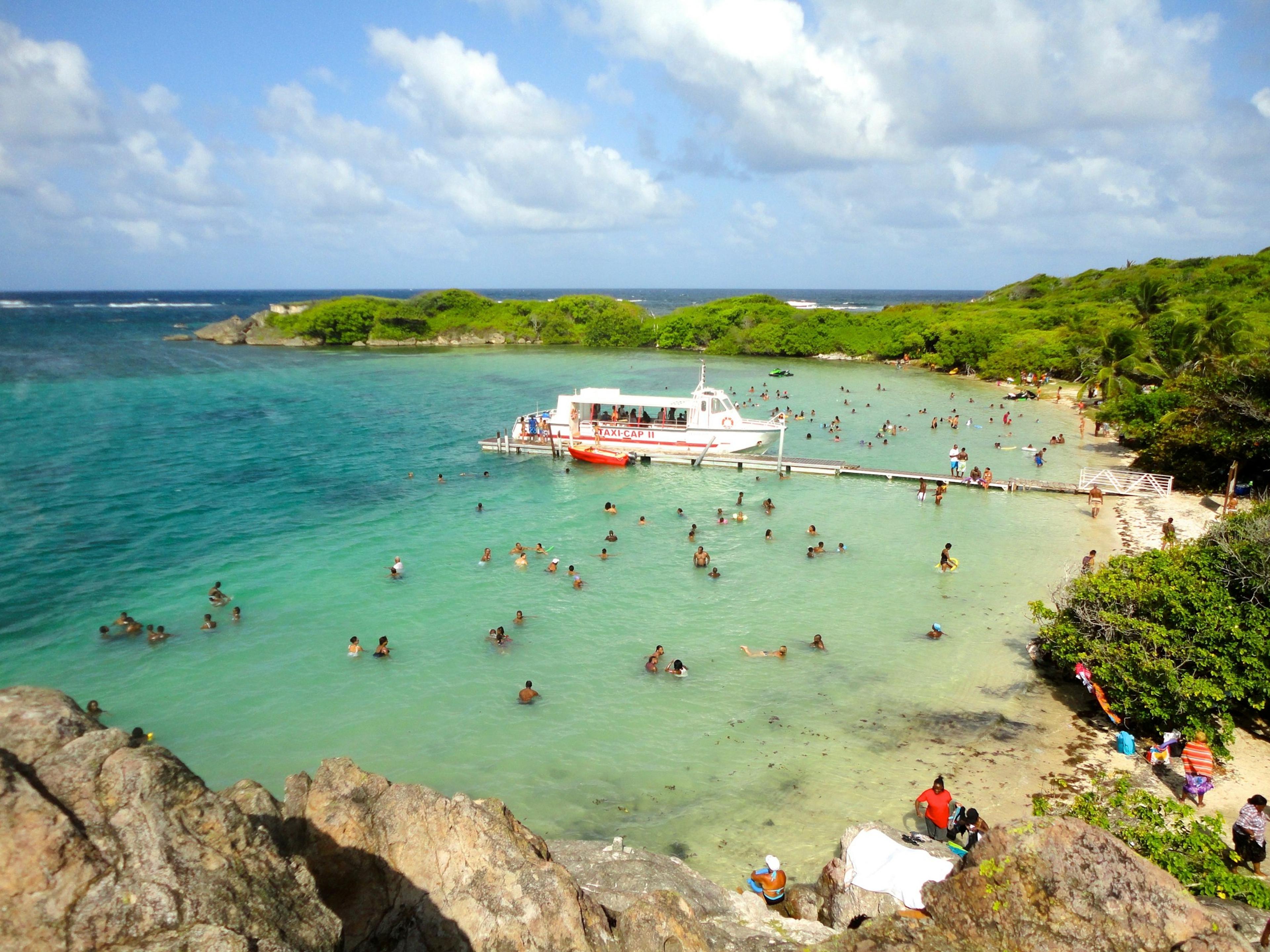 Swimmers in clear water around a small island, a boat at anchor