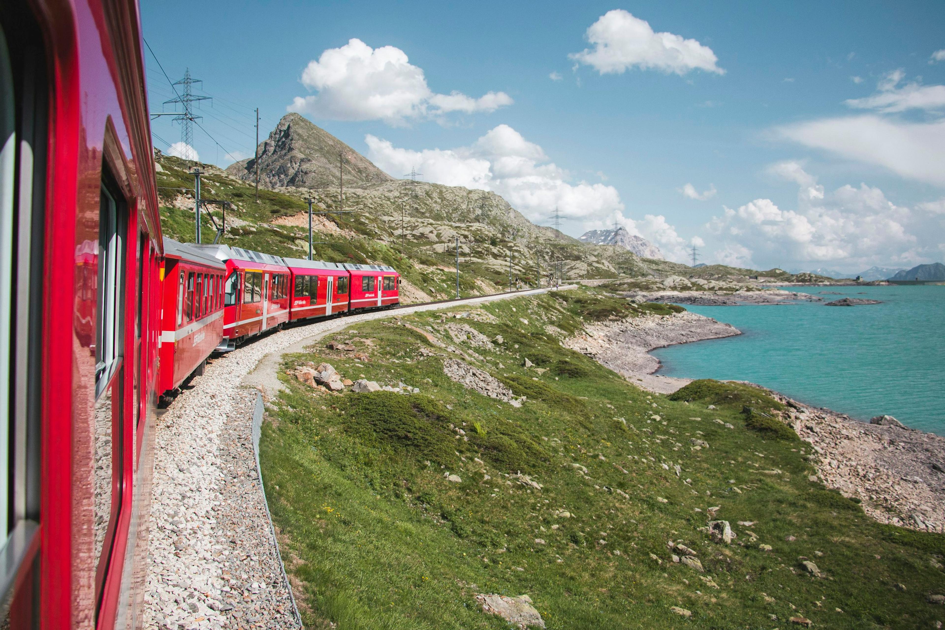 Un train rouge longe un lac turquoise au milieu des montagnes
