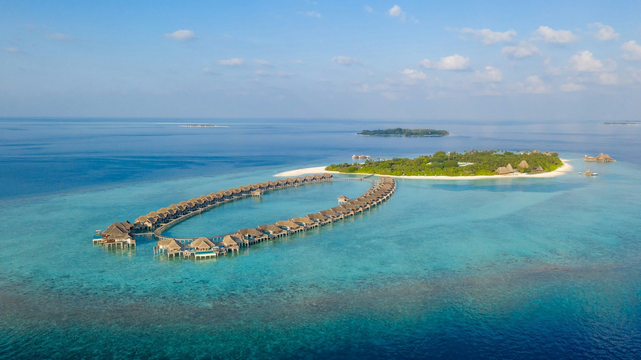 Des bungalows sur pilotis dessinent un arc dans le lagon, devant une île