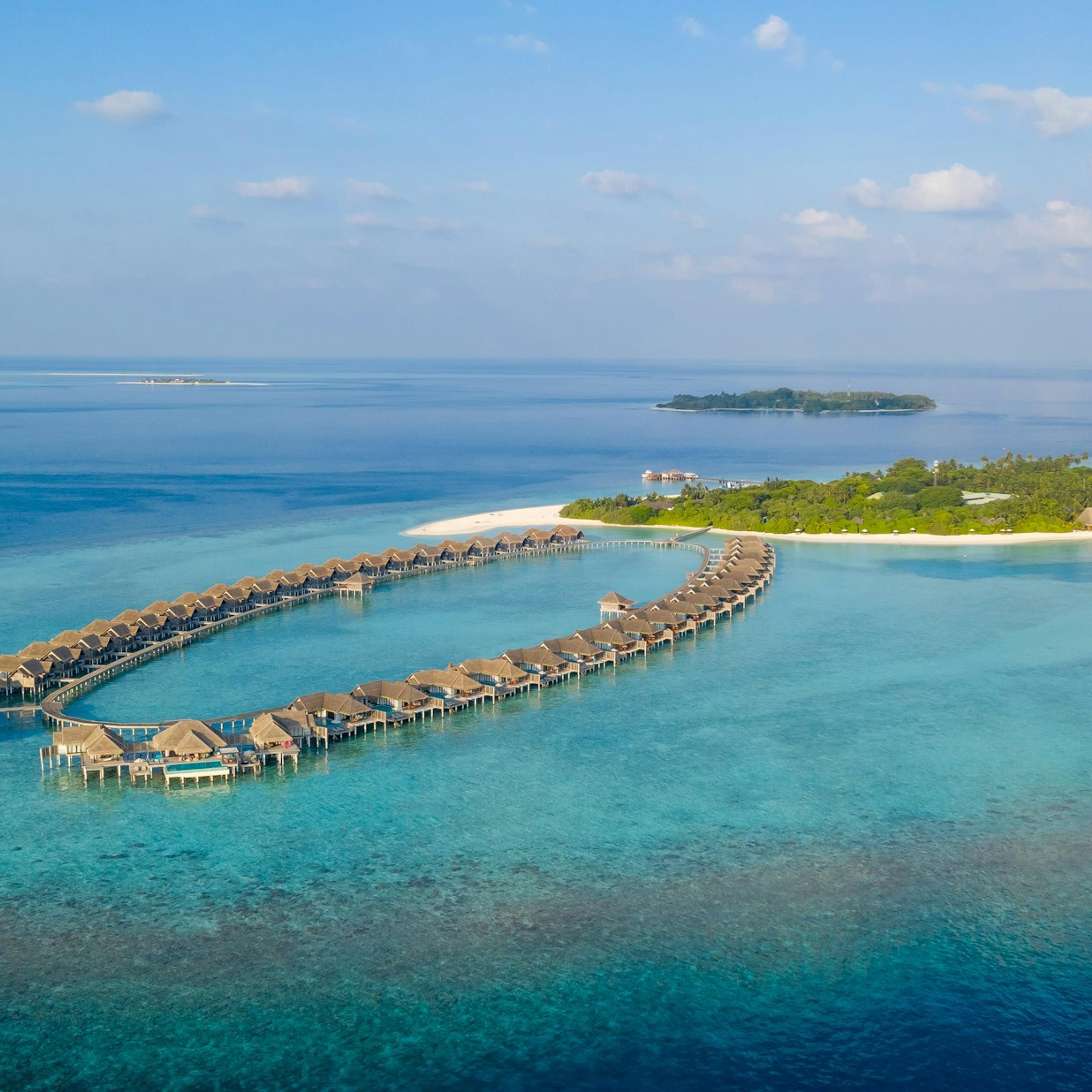 Des bungalows sur pilotis dessinent un arc dans le lagon, devant une île