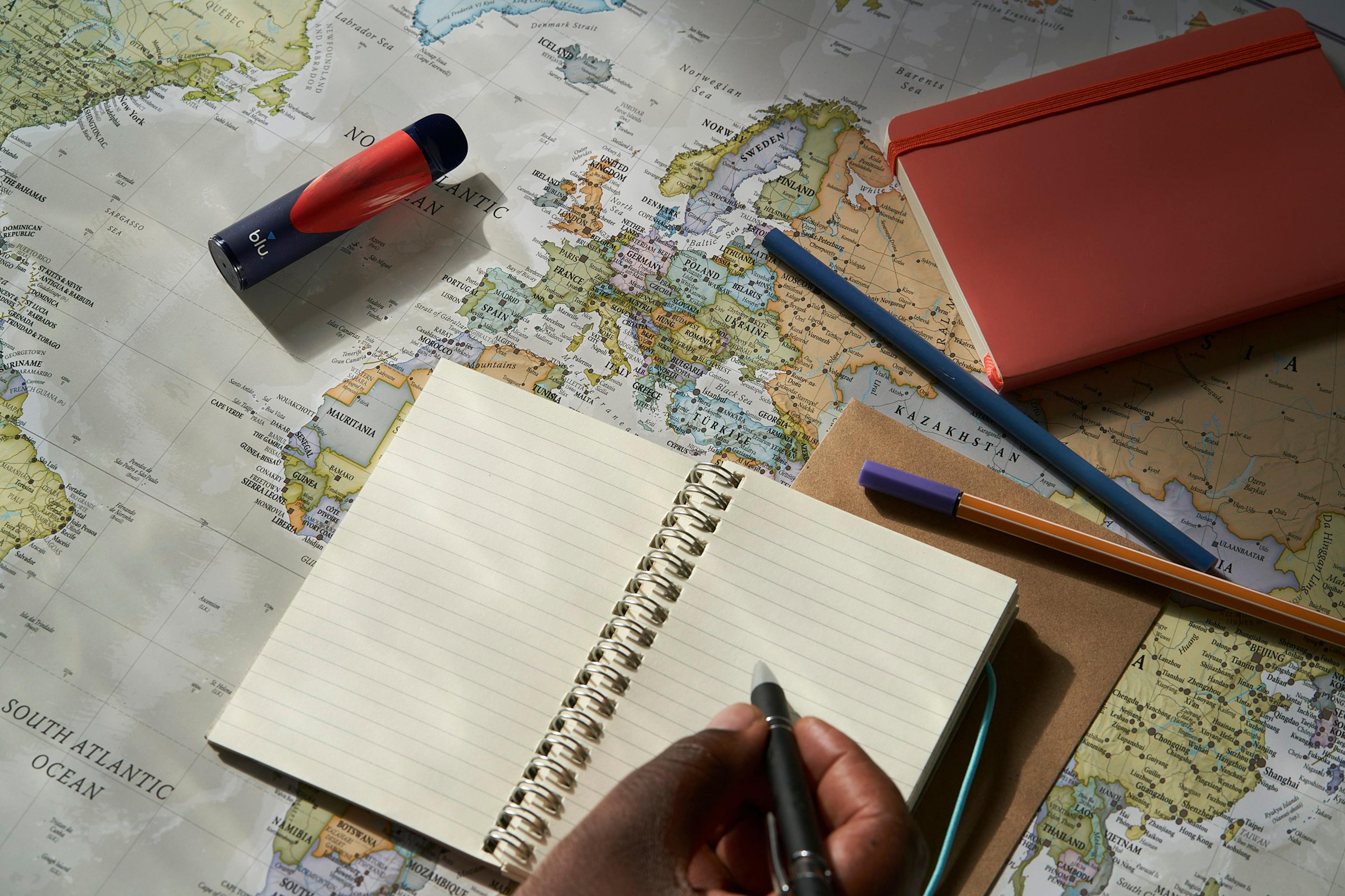 Un carnet ouvert et des crayons posés sur une carte du monde