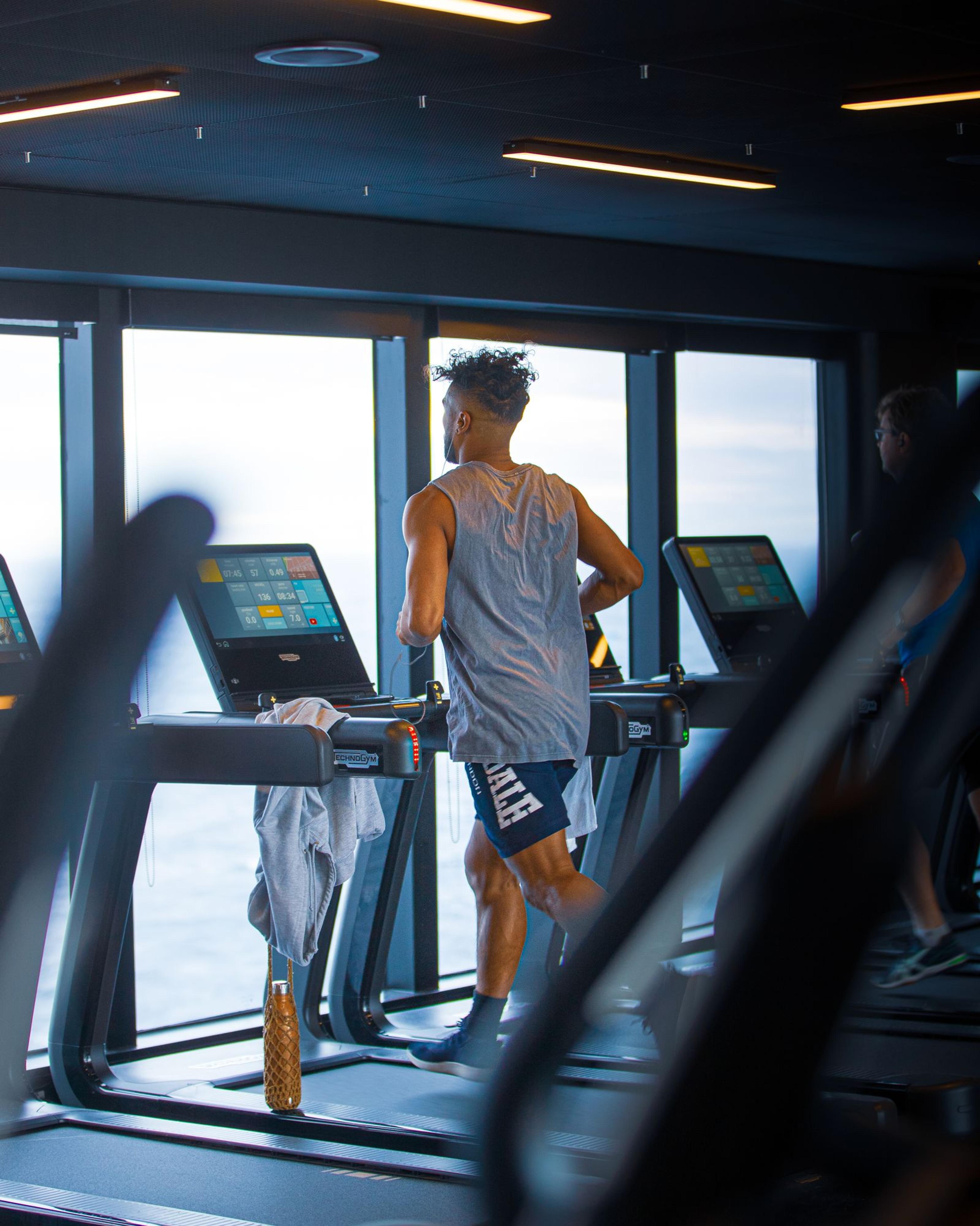 Un passager court sur un tapis roulant dans la salle de cardio, devant les baies vitrées