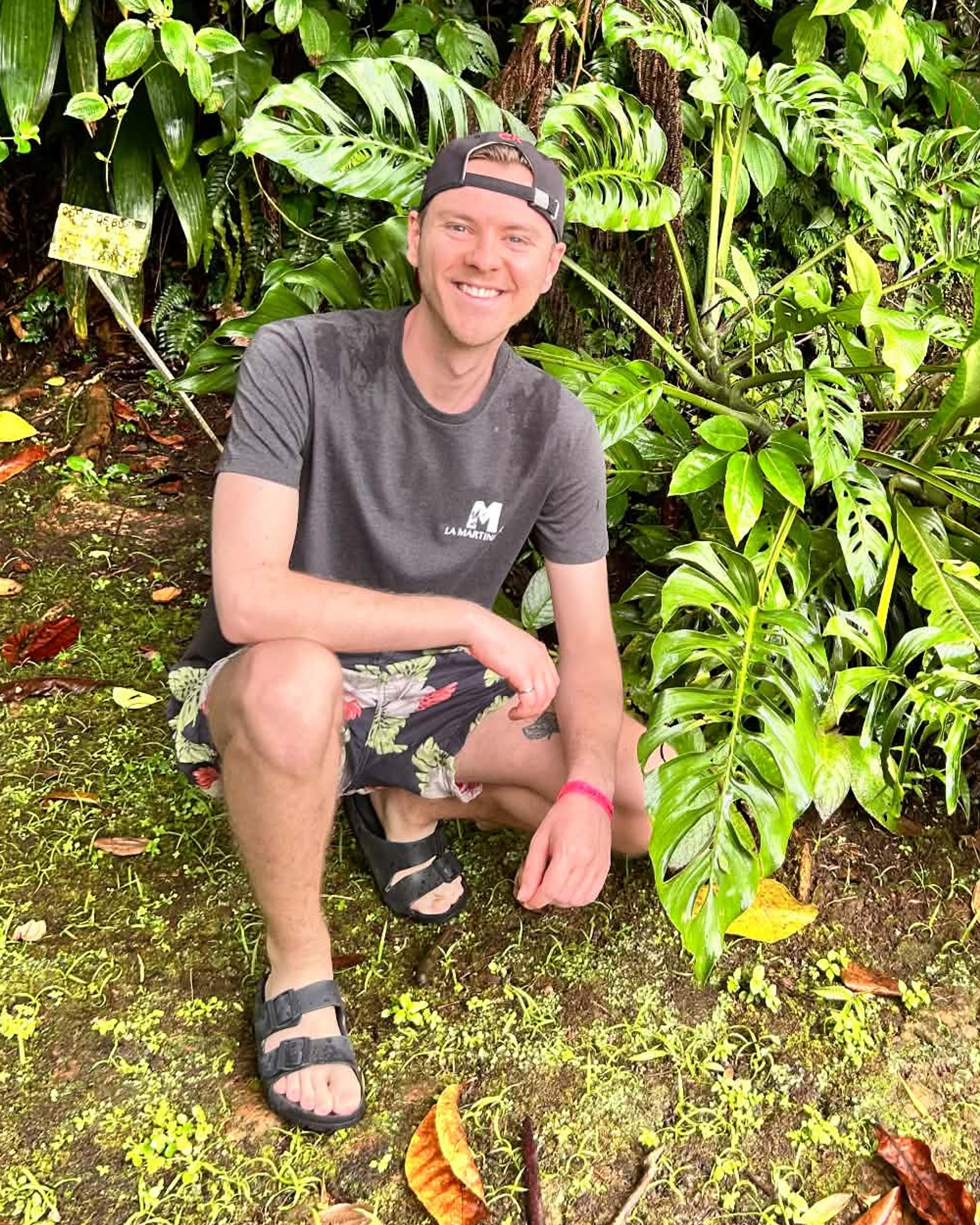 Jérémie Lesuise, souriant, accroupi devant une végétation tropicale