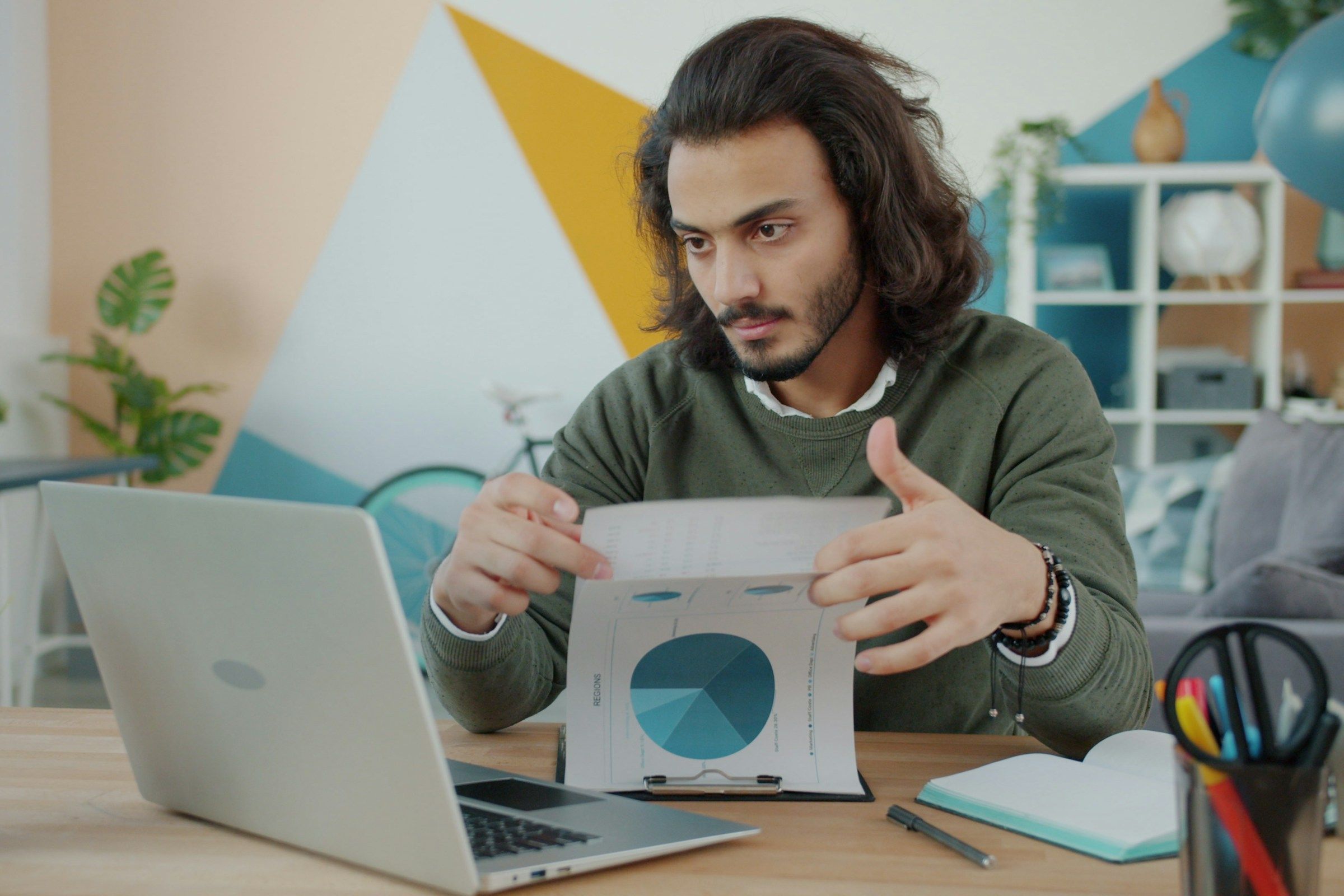 Man looking at laptop and paper in colorful room