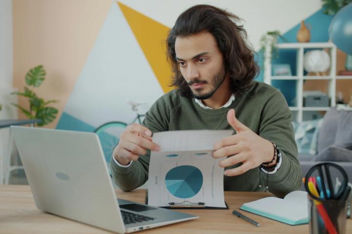 Man looking at laptop and paper in colorful room