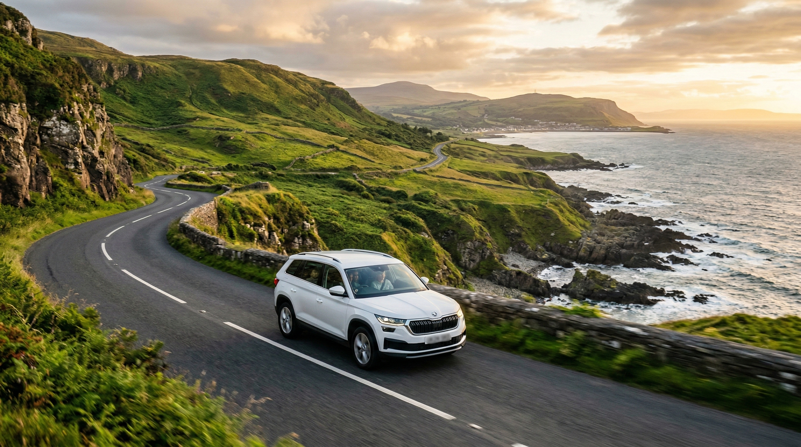 Modern SUV driving along the scenic Causeway Coastal Route in Northern Ireland at golden hour, with dramatic cliffs and the Atlantic Ocean in the background.
