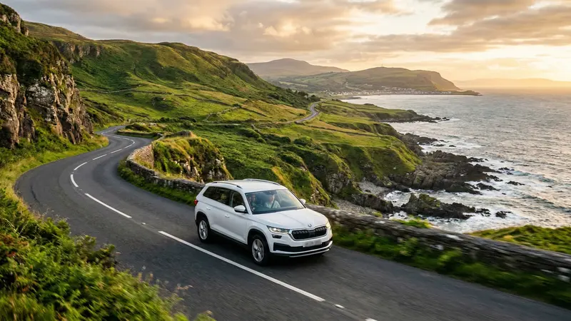 Modern SUV driving along the scenic Causeway Coastal Route in Northern Ireland at golden hour, with dramatic cliffs and the Atlantic Ocean in the background.