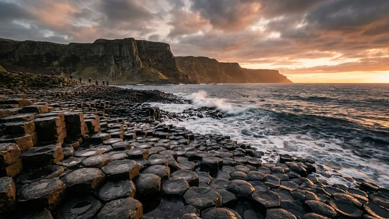 Dramatic view of the Giant's Causeway basalt columns at sunset, with waves crashing against the coast.