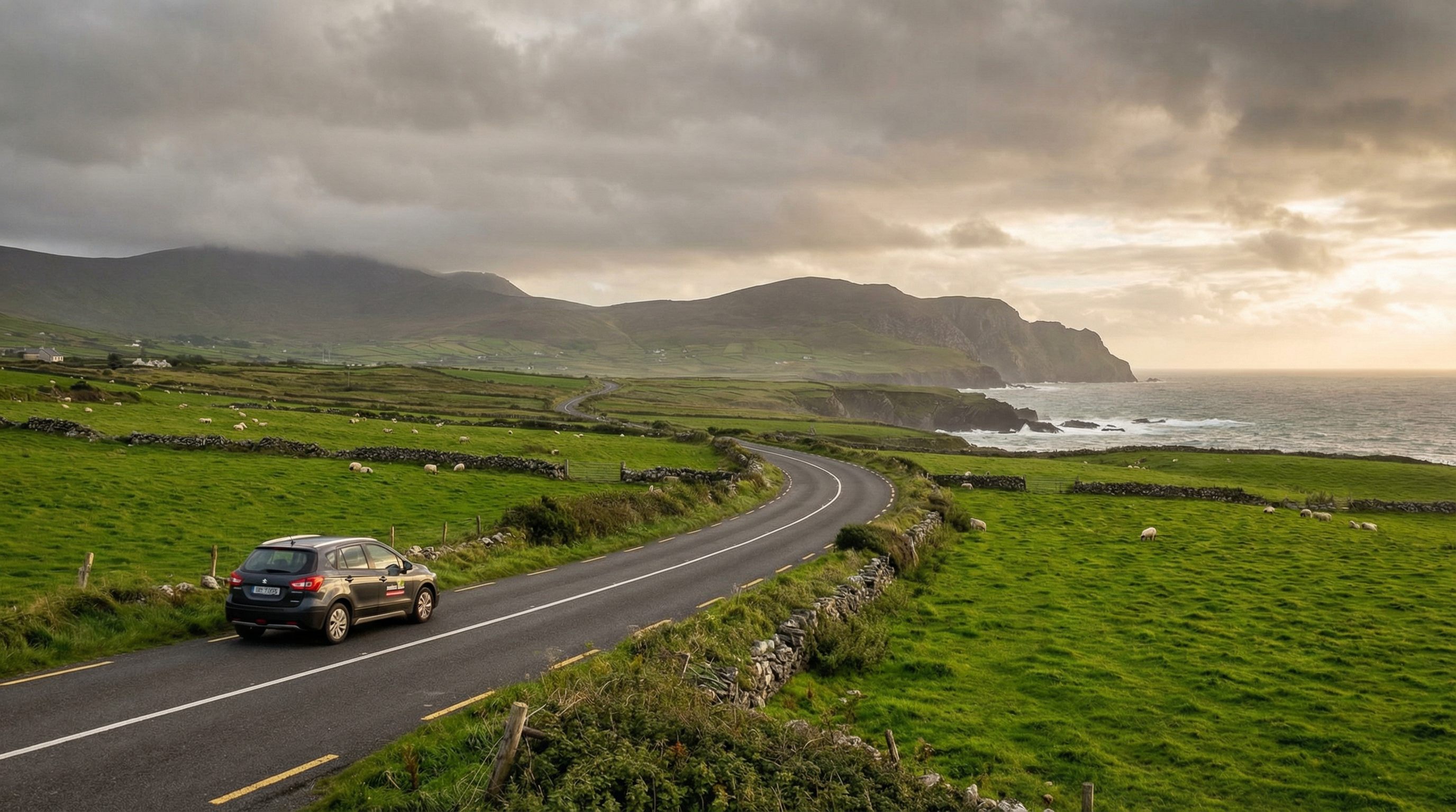 A modern rental car drives along a dramatic coastal road in Ireland at golden hour, with lush green fields and the Atlantic Ocean in the background.
