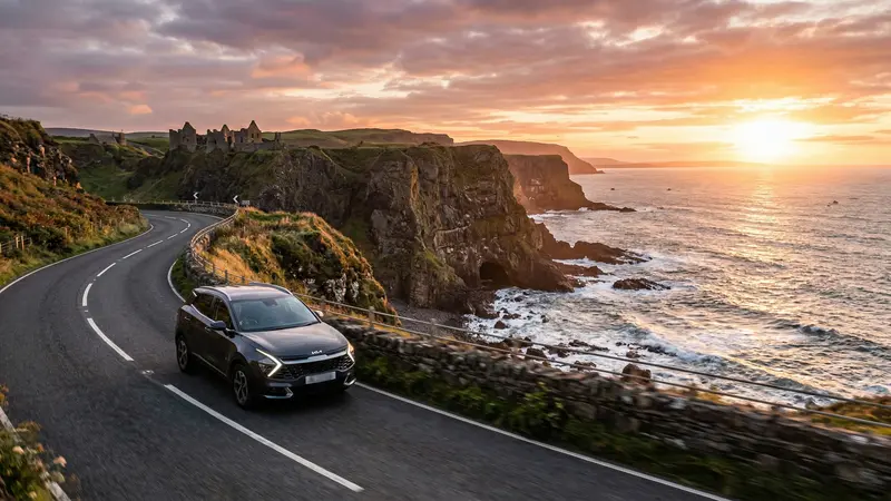 Modern SUV driving along the scenic Causeway Coastal Route in Northern Ireland at sunset