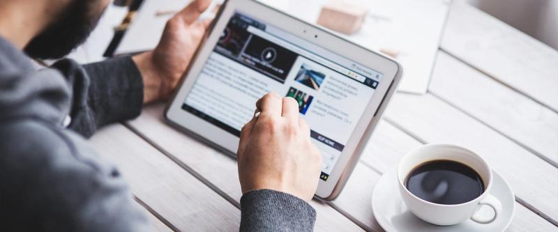Person reading a news article on a tablet at a table with coffee