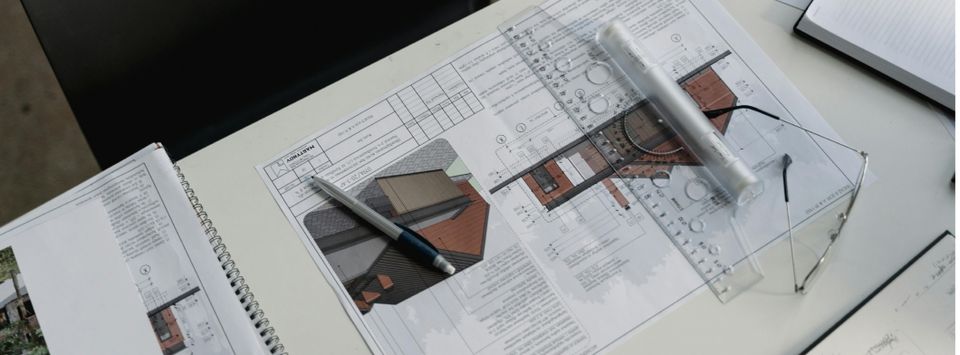 Architectural floor plans on a desk with a pen, ruler and glasses