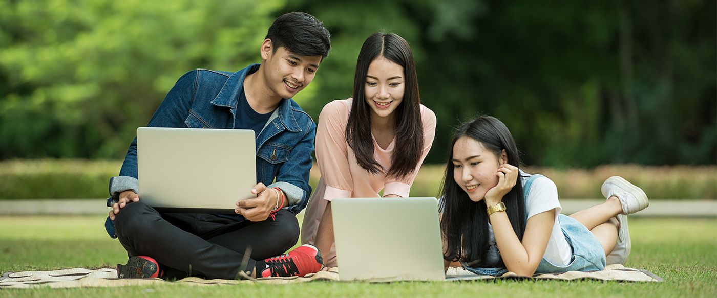 Three young people sit outdoors sharing laptops in a collaborative moment