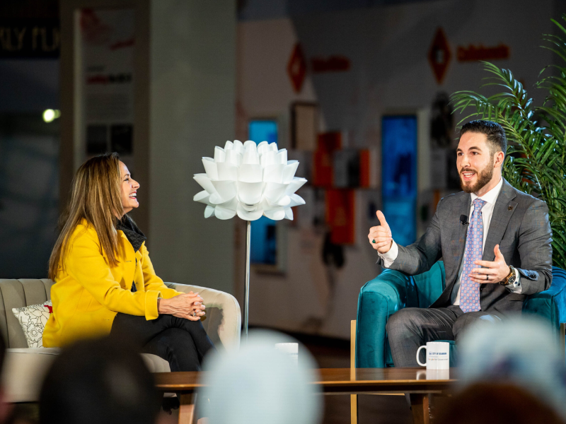 Two people talking on a stage in front of a seated audience