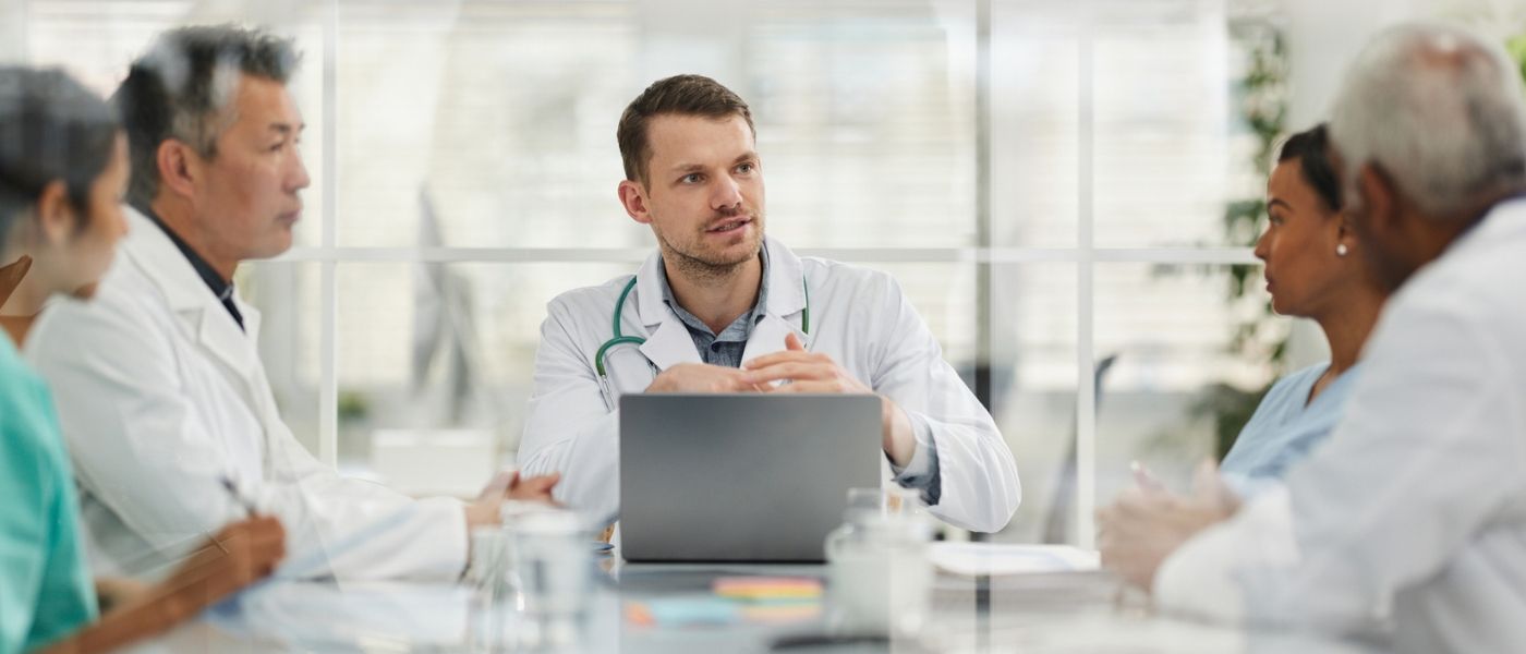 A doctor leading a discussion with colleagues around a laptop in a meeting room