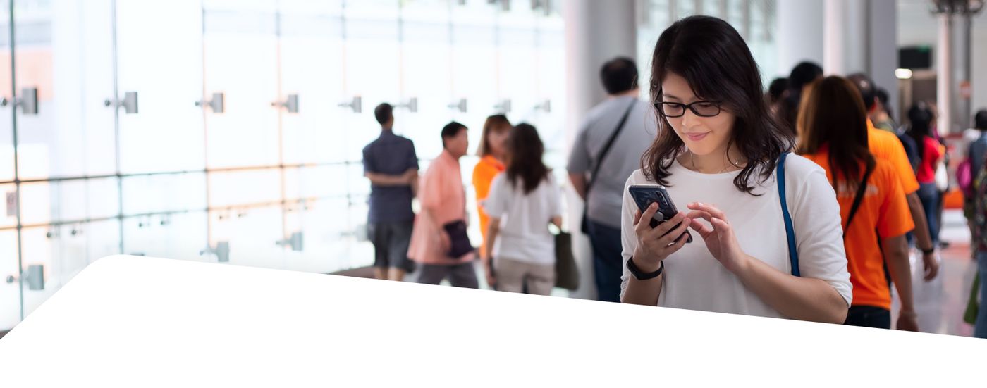 Commuter checking her phone in a busy MTR station concourse
