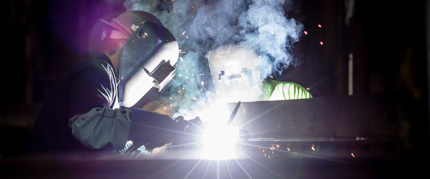 A welder works with sparks flying while wearing protective gear