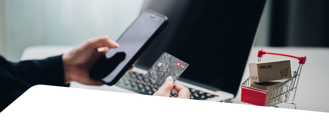 Shopper holding an HSBC card while checking out on a laptop, with a mini shopping cart nearby