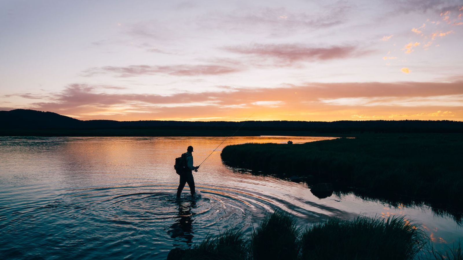 Angler fly fishing in a river at sunset