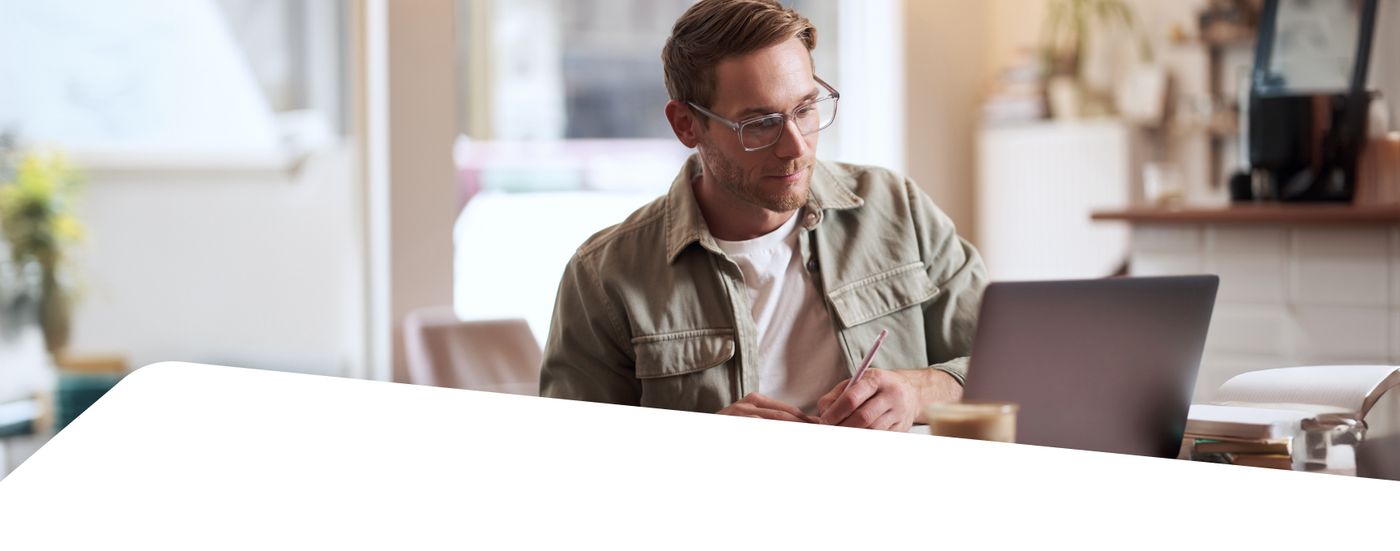 A man wearing glasses works at a laptop in a home office