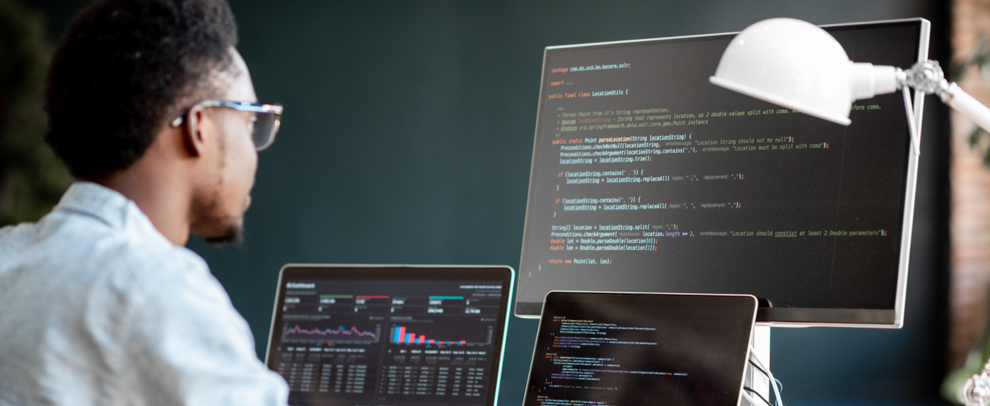 A developer reviews code and a data dashboard across multiple monitors