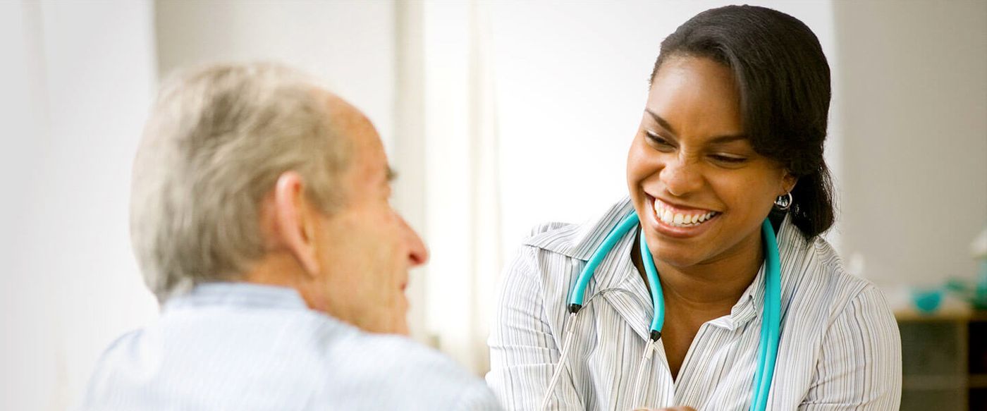 Smiling healthcare worker with a stethoscope talking with an elderly patient