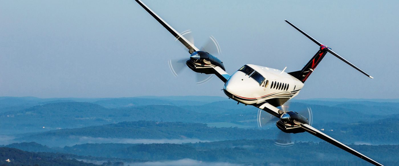A twin-engine turboprop aircraft flies over hazy hills