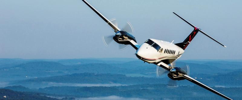 A twin-engine turboprop aircraft flies over hazy hills
