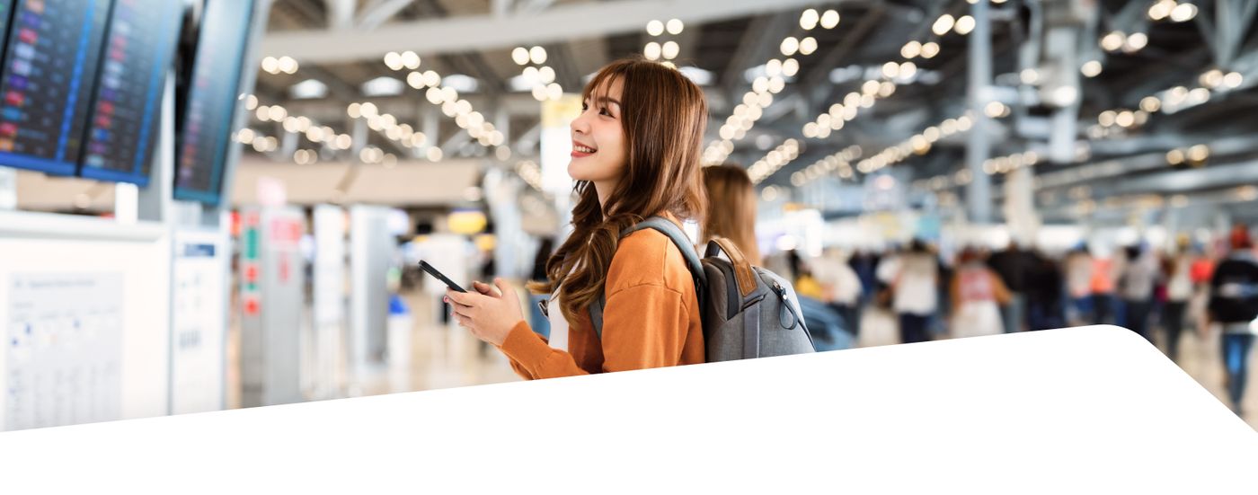 Traveler checking her phone in an airport terminal near a flight information board