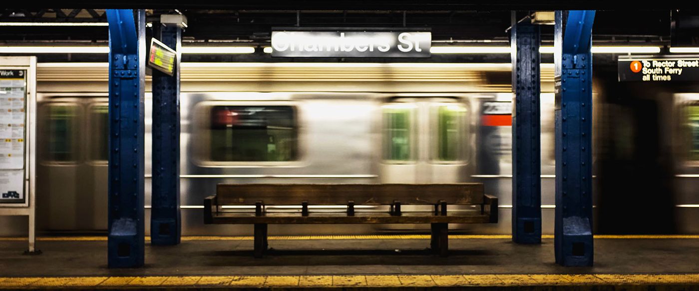 A subway train blurs past an empty bench at the Chambers Street station