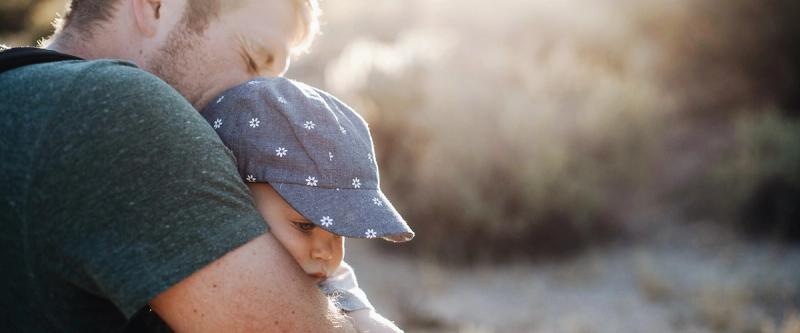 A father carries his young child outdoors in golden afternoon light