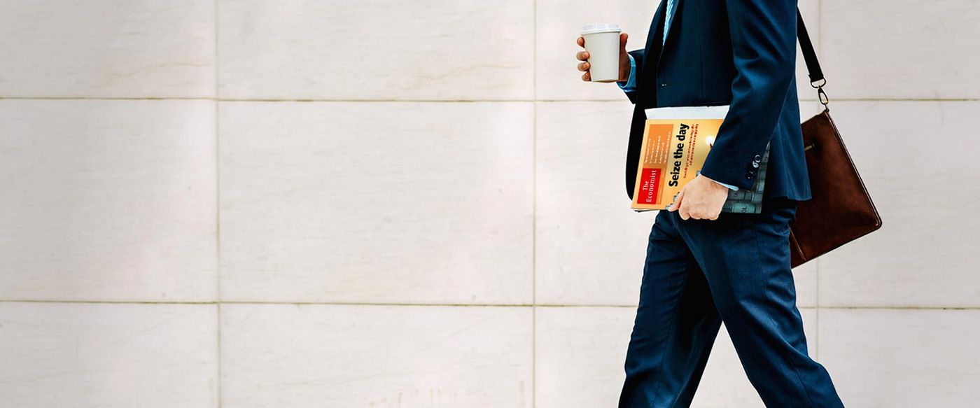A businessman walks by carrying a coffee cup and a book titled 'Seize the day'